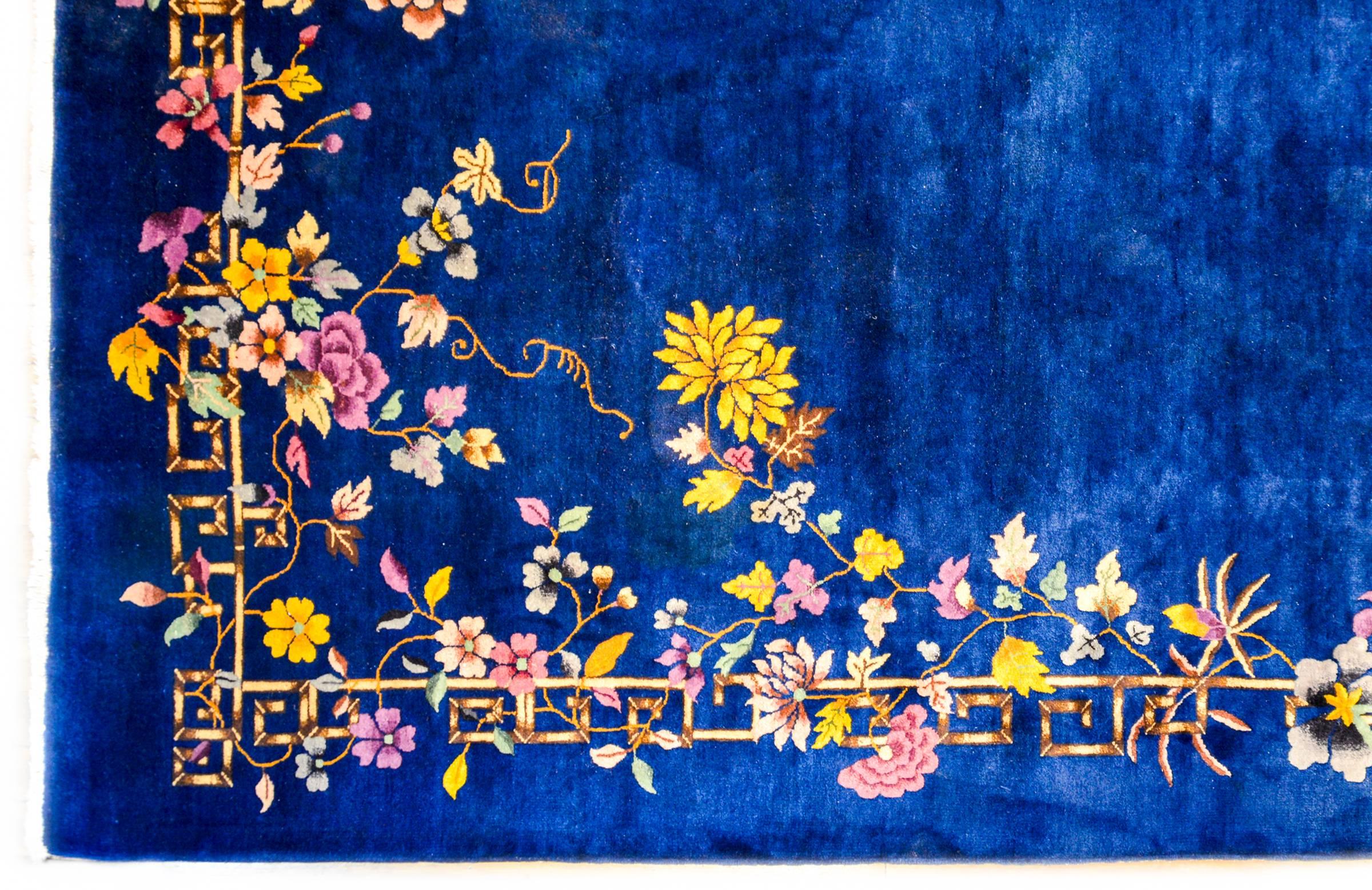 A fabulous early 20th century Chinese Art Deco rug with a rich deep indigo background surrounded by a stylized-dragon bamboo motif border, with multiple multicolored auspicious Chinese flowers including peonies, chrysanthemums, lotus and prunus.