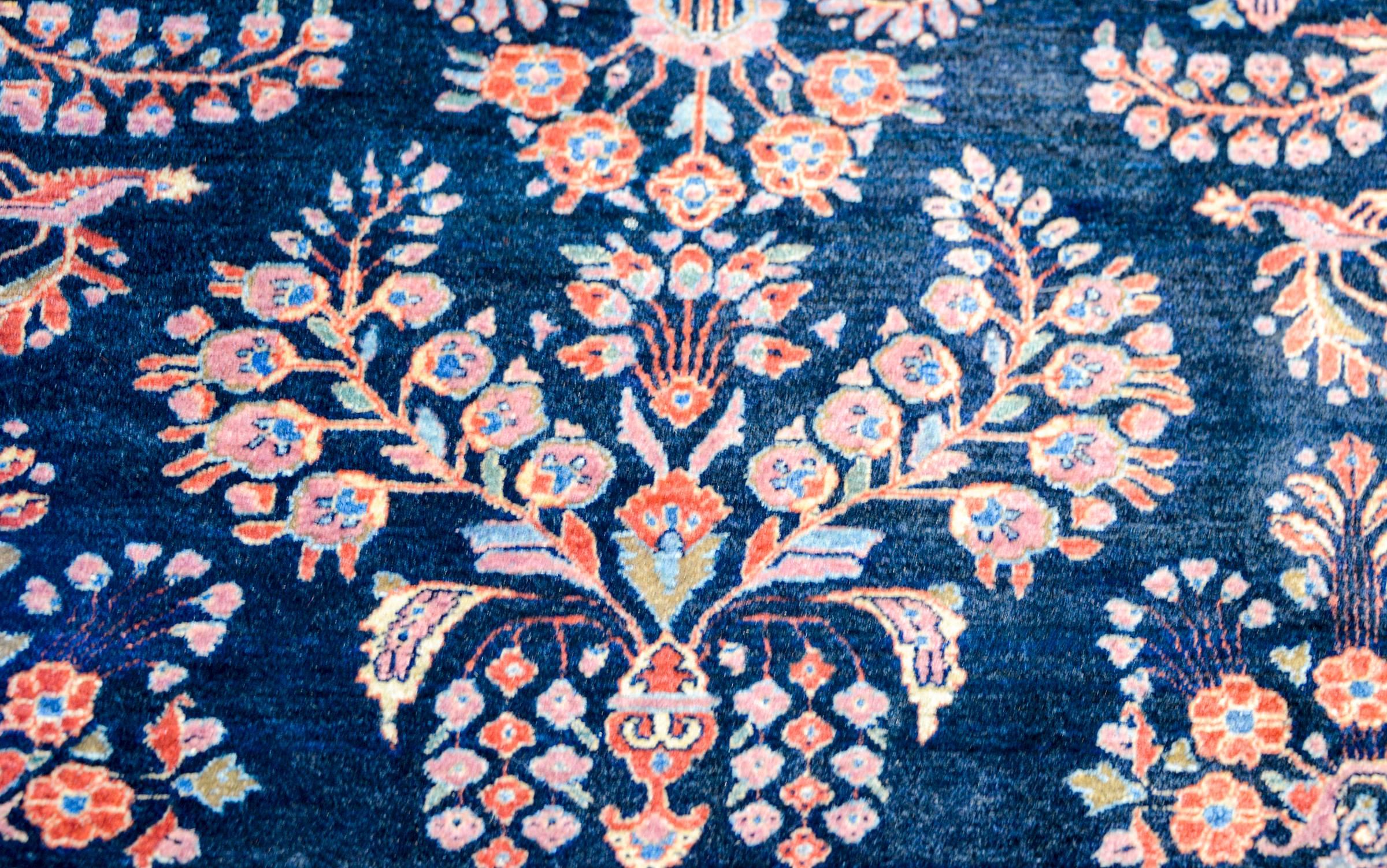 A wonderful and Classic early 20th century Persian Sarouk Mohajeran rug with a traditional mirrored floral pattern woven in crimson, pink, and light indigo, on a dark indigo background. The border is contrasting with a wide cranberry stripe with a