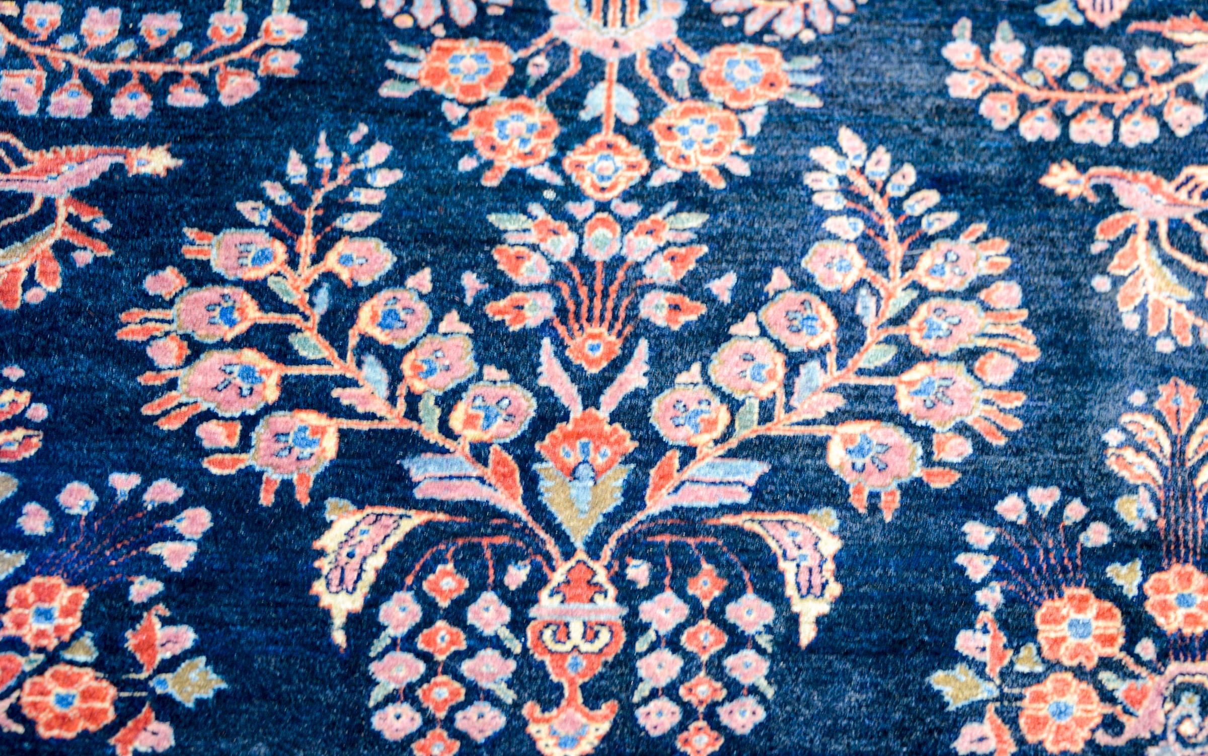 Un meraviglioso e classico tappeto persiano Sarouk Mohajeran dell'inizio del XX secolo con un tradizionale motivo floreale a specchio tessuto in cremisi, rosa e indaco chiaro, su uno sfondo indaco scuro. Il bordo è a contrasto con un'ampia striscia