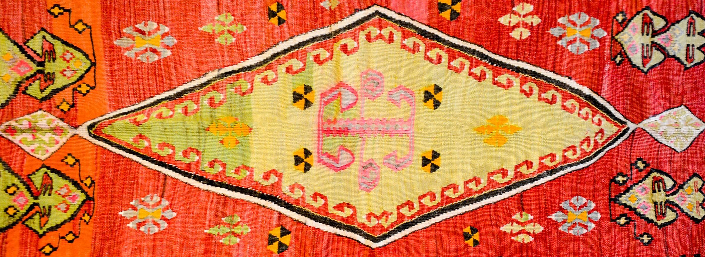 An early 20th century Turkish Kilim rug with a brilliant spring green diamond medallion amidst a field of geometric stylized flowers on a crimson background. The border is wide composed two stripes, the same width, one with stylized flowers on a