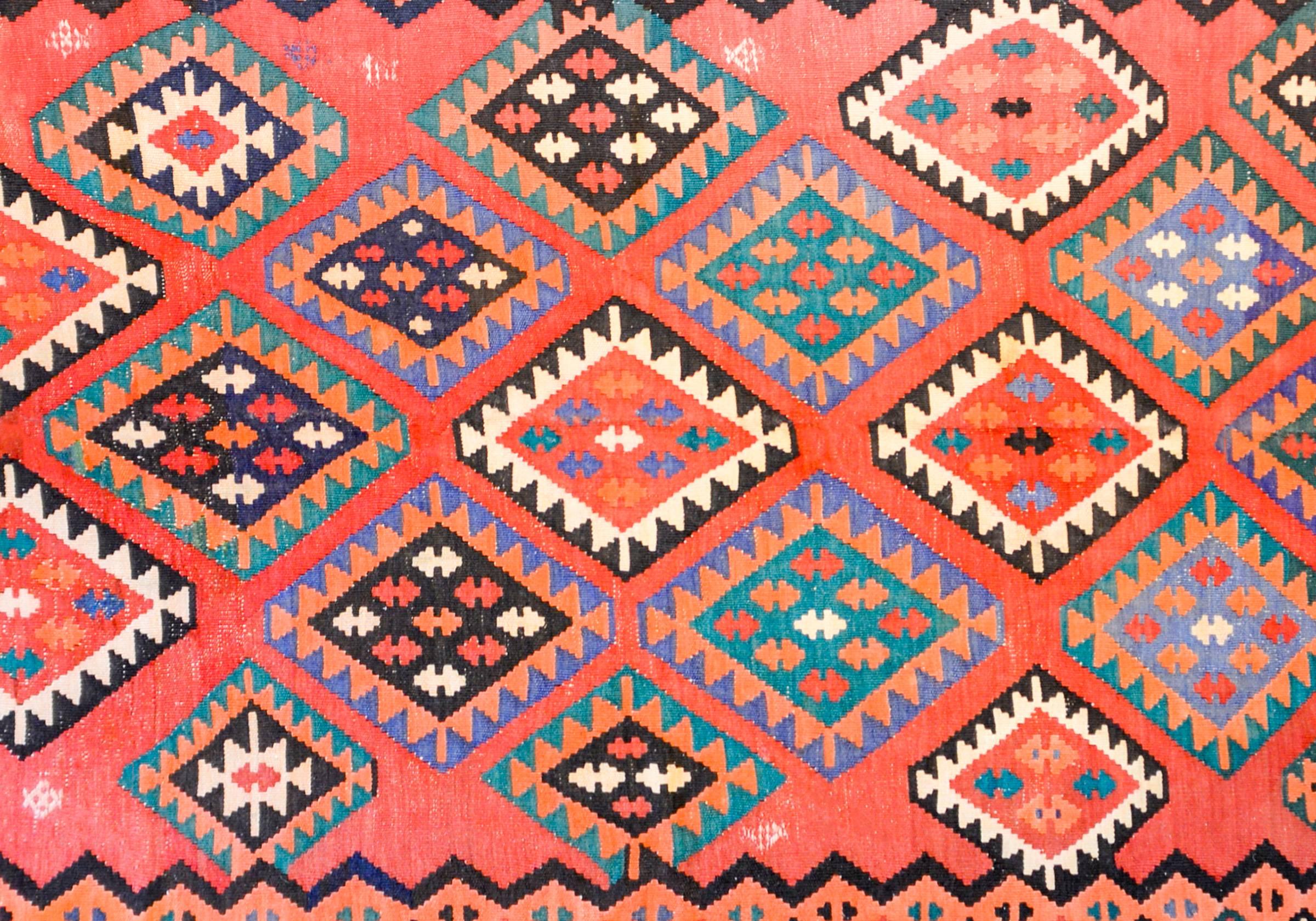 Un fantastique tapis de course Persan Qazvin du début du 20ème siècle avec un magnifique motif de diamants multicolores tissés en orange, lavande, noir et blanc sur un fond cramoisi pâle. La bordure est complémentaire avec un large motif géométrique