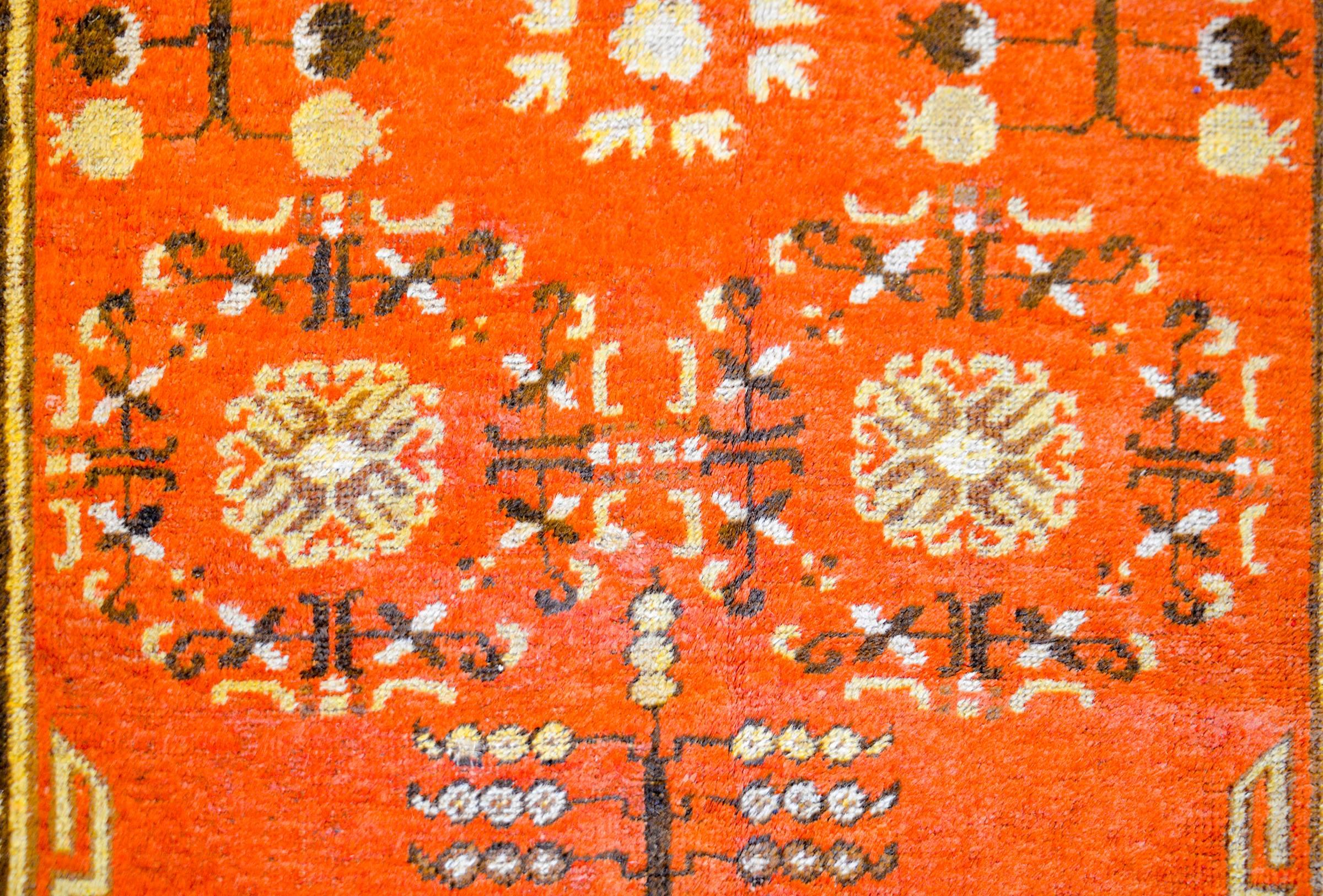 An early 20th century Central Asian Khotan rug with a beautiful orange field of pomegranate, trees-of-life, and floral patterns. The border is wonderfully rendered consisting of Buddhist endless knot patterns, turbulent clouds, and stepped rays of