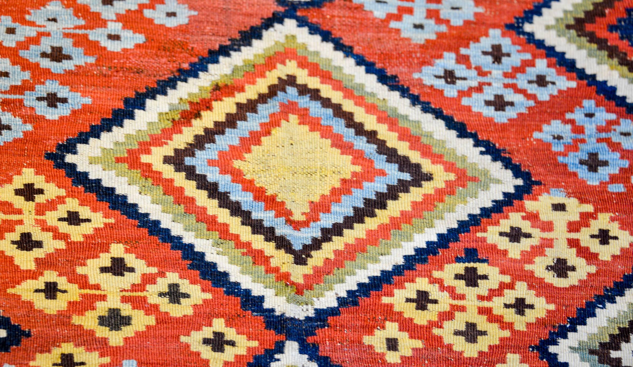 An incredible mid-20th century Persian Ghashgaei kilim with a beautiful asymmetrical woven pattern containing three large diamond medallions each composed of multiple multicolored stripes amidst a field of multicolored flowers on a crimson