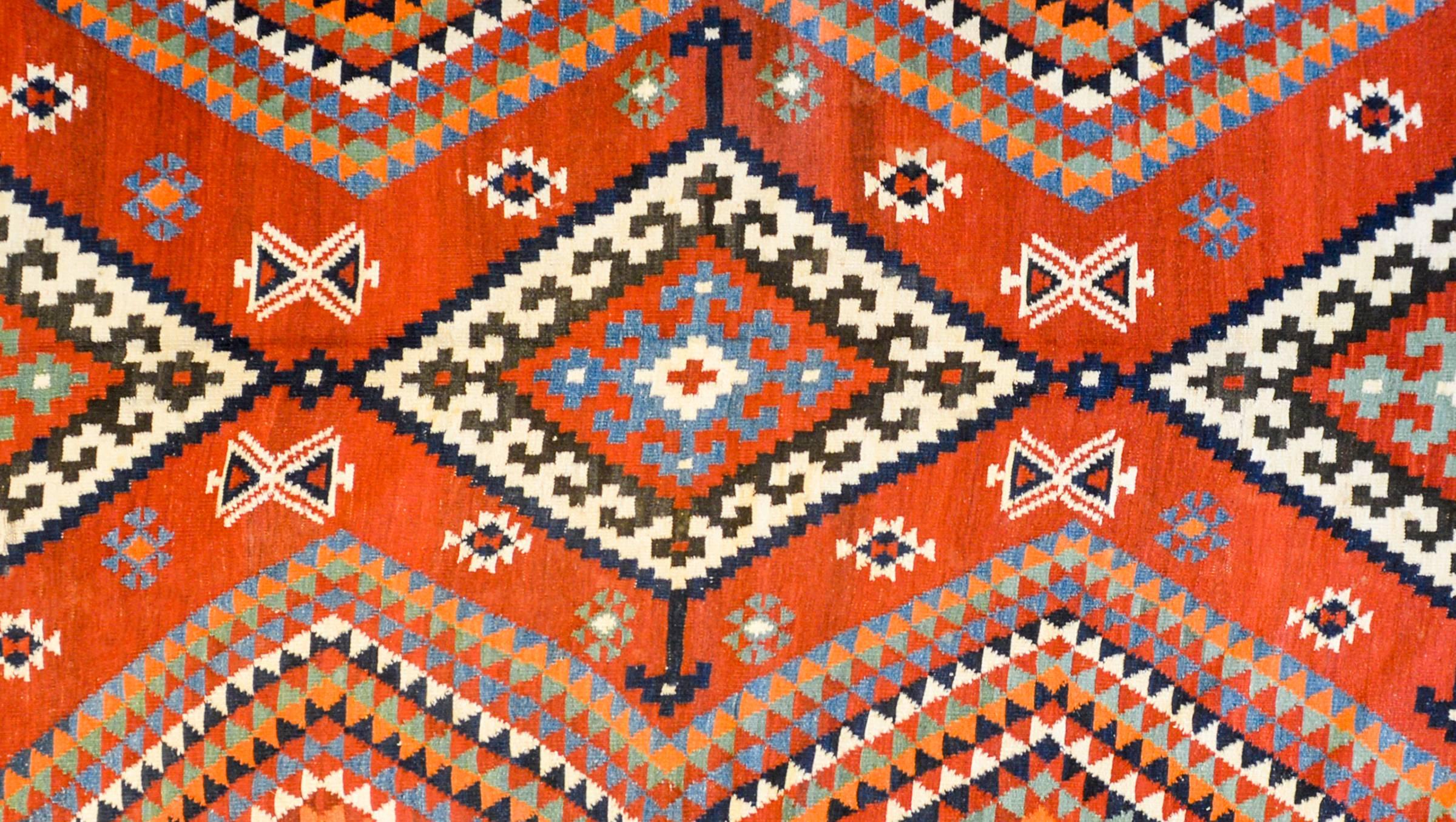 A beautiful mid-20th century Persian Harsin Kilim rug with three large diamond medallions each with a geometric flowers in the center, all on a crimson field of stylized flowers. Beautiful multicolored triangle stripes zigzag up the sides. The