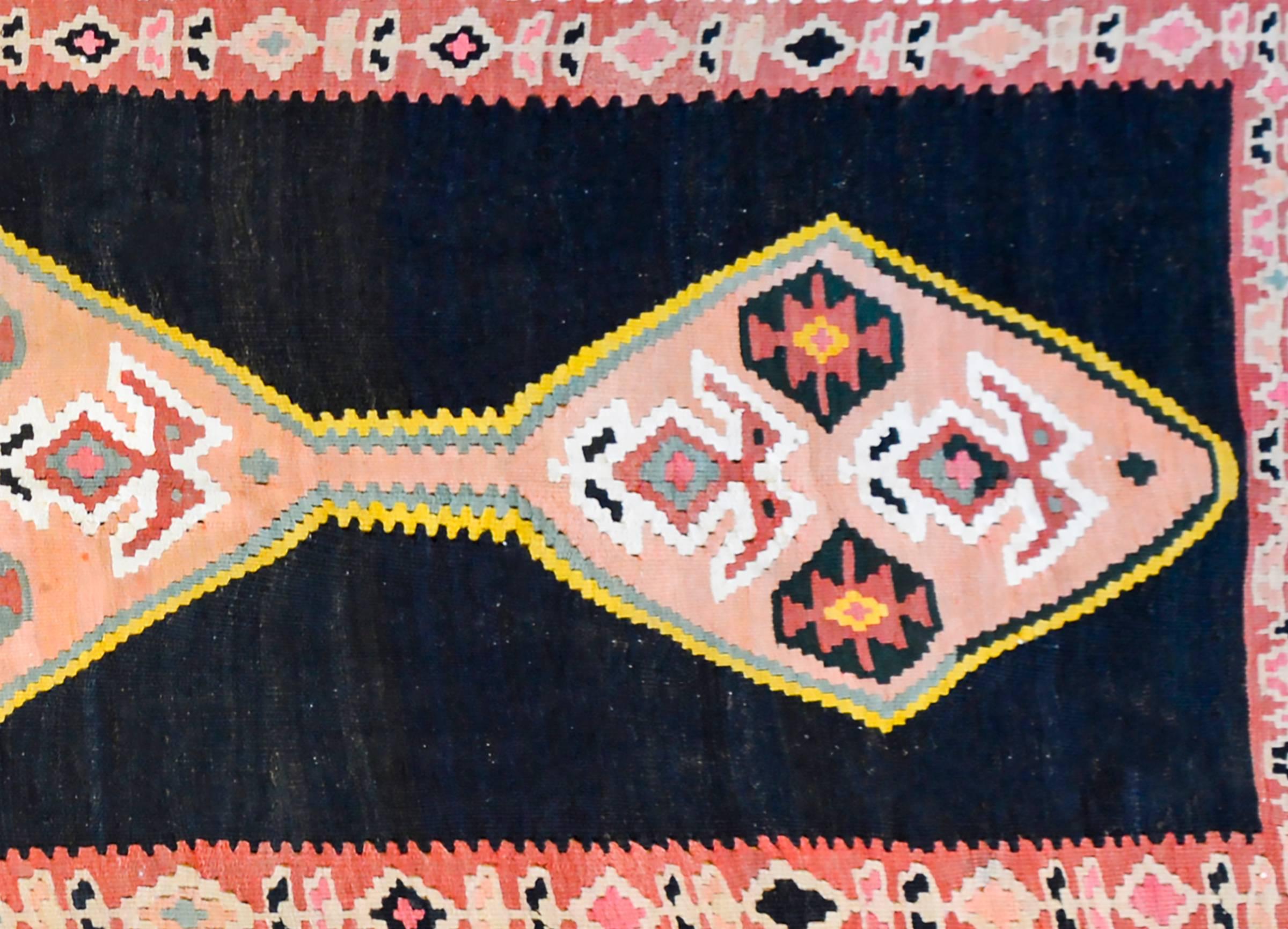 A wonderfully bold Late 20th century Persian Zanjan Kilim rug with three large diamond medallions each with stylized flowers, on an abrash orange background outlined by pale blue and gold stripes. The background is a deep, almost black, indigo. The