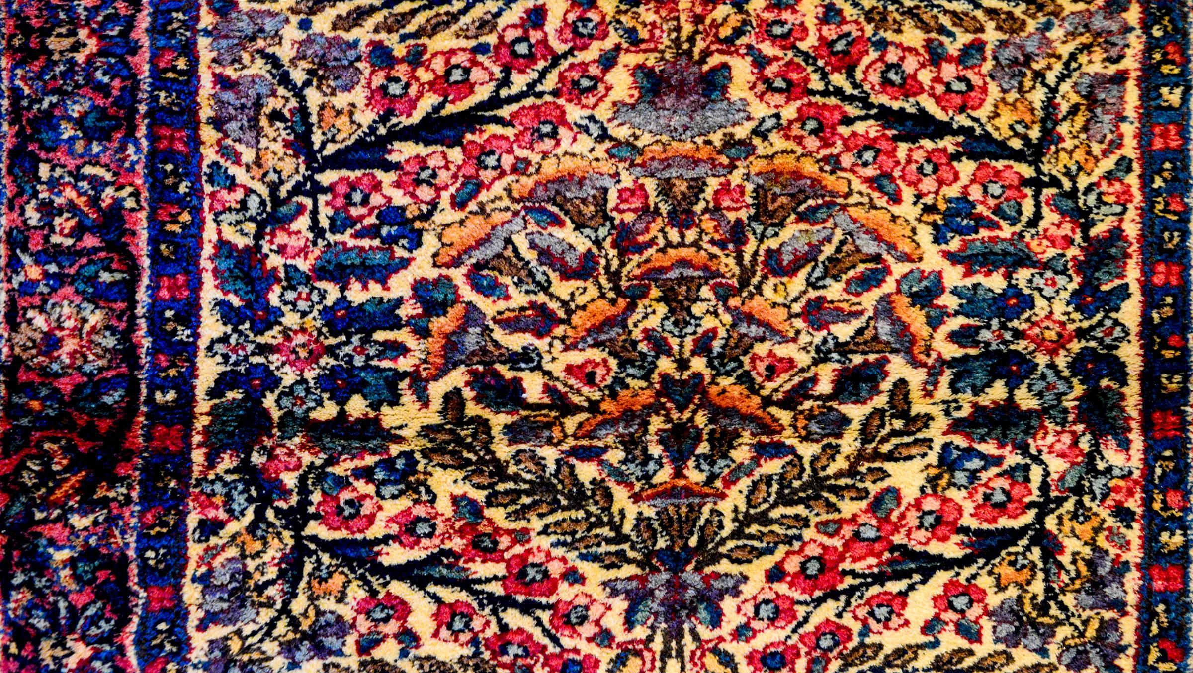 A wonderful early 20th century Persian Kirman rug with a densely woven mirrored floral and leaf pattern woven in indigo, pink, gold and green vegetable dyed wool. The border is contrasting with a wide floral and vine patterned band flanked by two