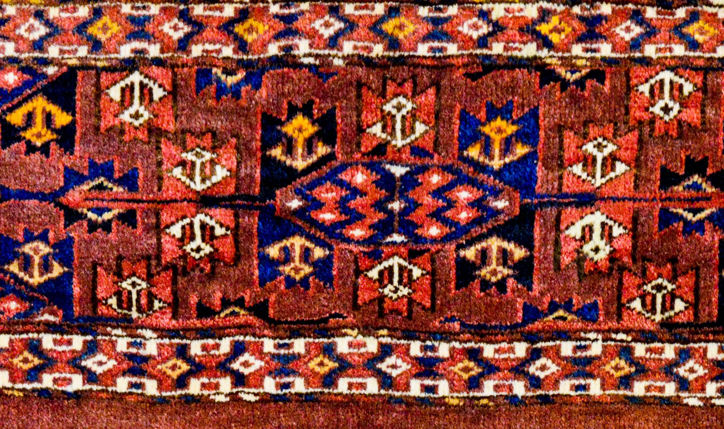 A beautiful 19th century Persian Yamut rug with an incredible geometric pattern woven in crimson, indigo, gold and natural brown wool. The border is contrasting is color, but similar in geometric style.