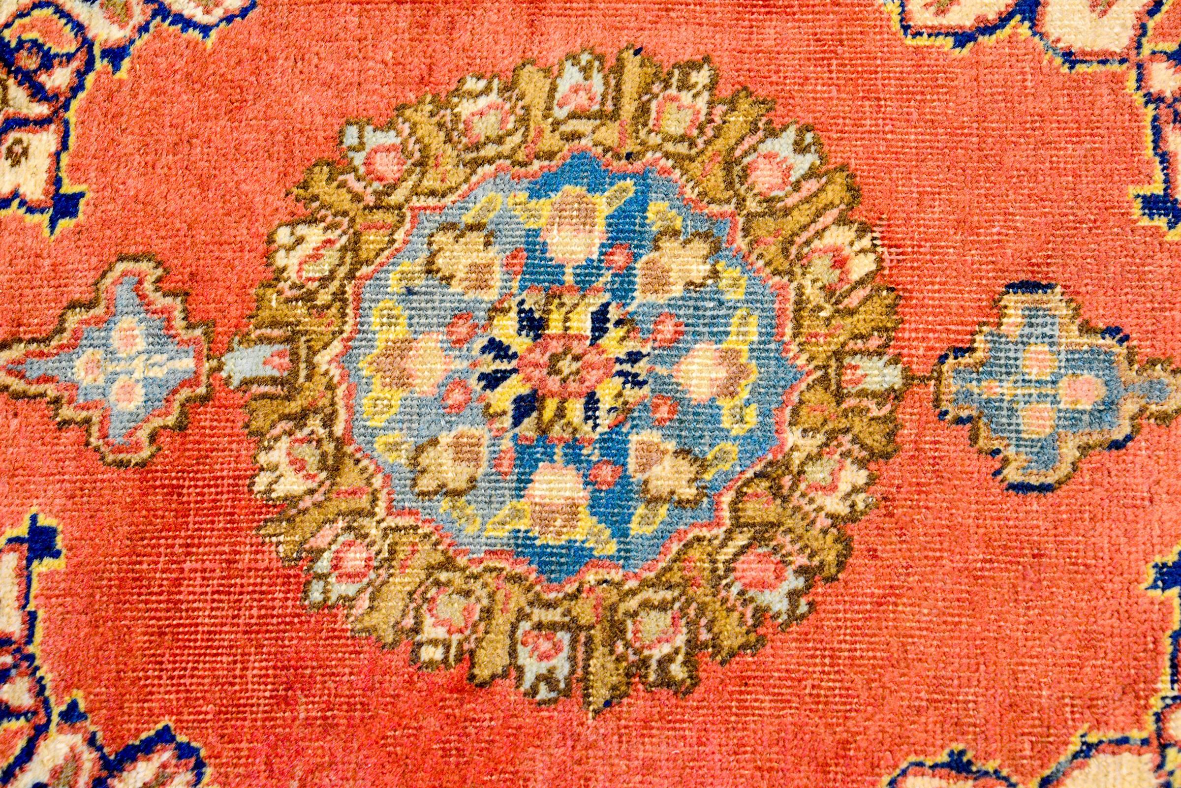 A wonderful early 20th century Persian Tabriz rug with a beautiful central floral medallion woven in indigo and gold, on a coral background. The border is sweet, with large-scale flowers and leaves.