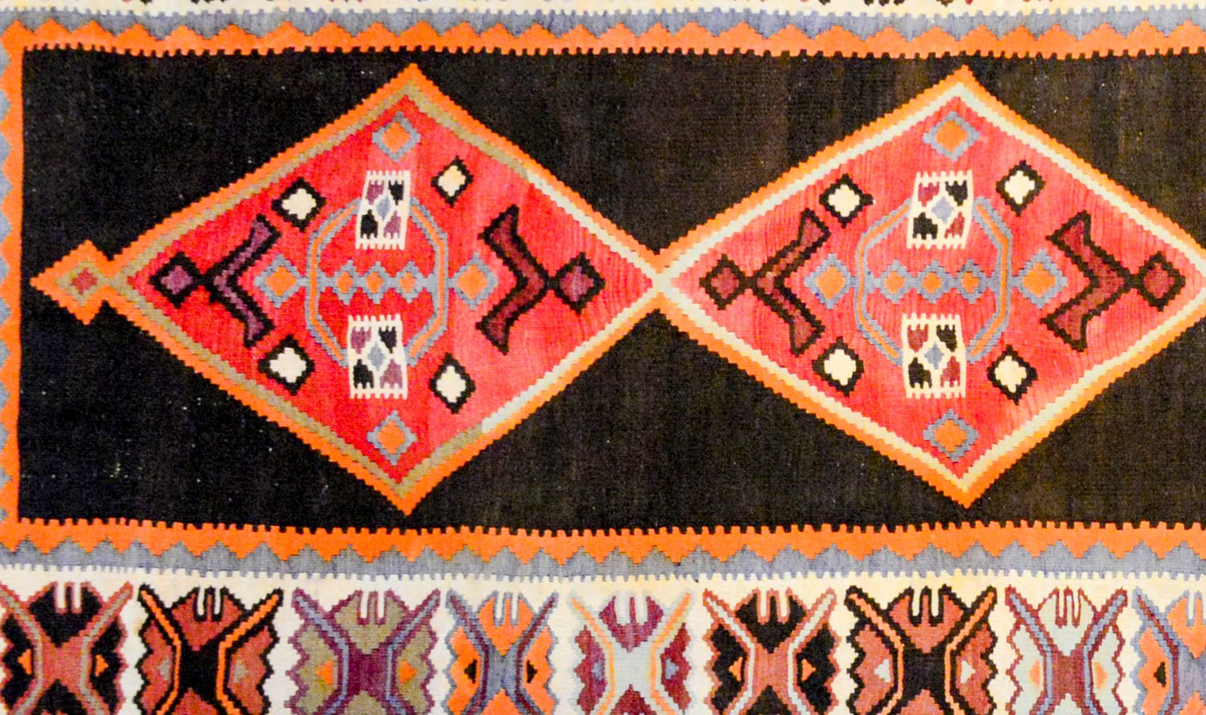 An early 20th century Persian Veramin Kilim runner with five large crimson diamond medallions on a black wool background surrounded by a wide border containing large-scale stylized floral shapes on a white background, with a thin outer border