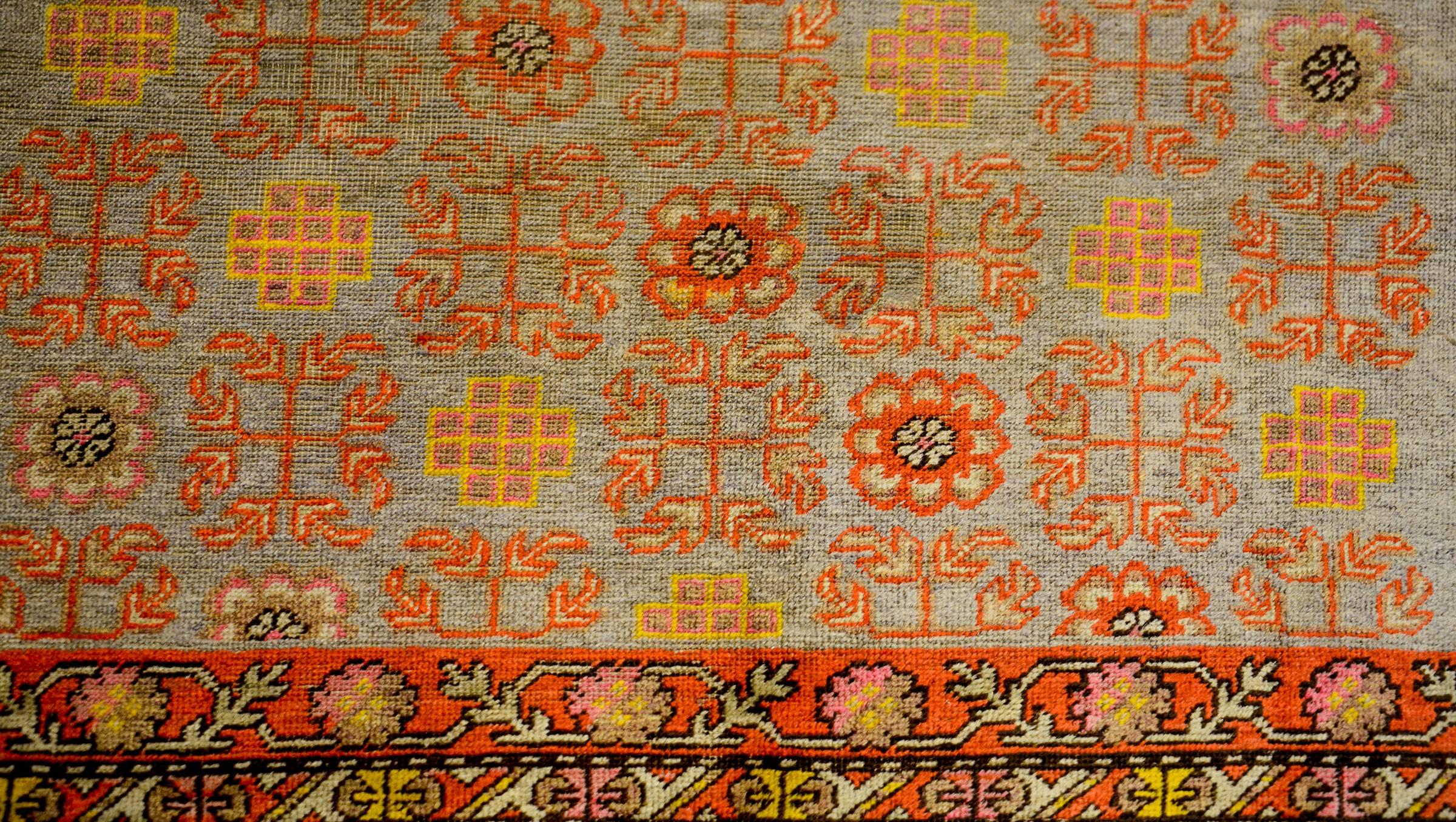 A wonderful early 20th century Central Asian Khotan rug with a beautiful all-over partern with alternating floral, leaf and endless-knot motifs, woven in rich crimson, gold, pink and green vegetable dyed wool, on a pale indigo background. The border