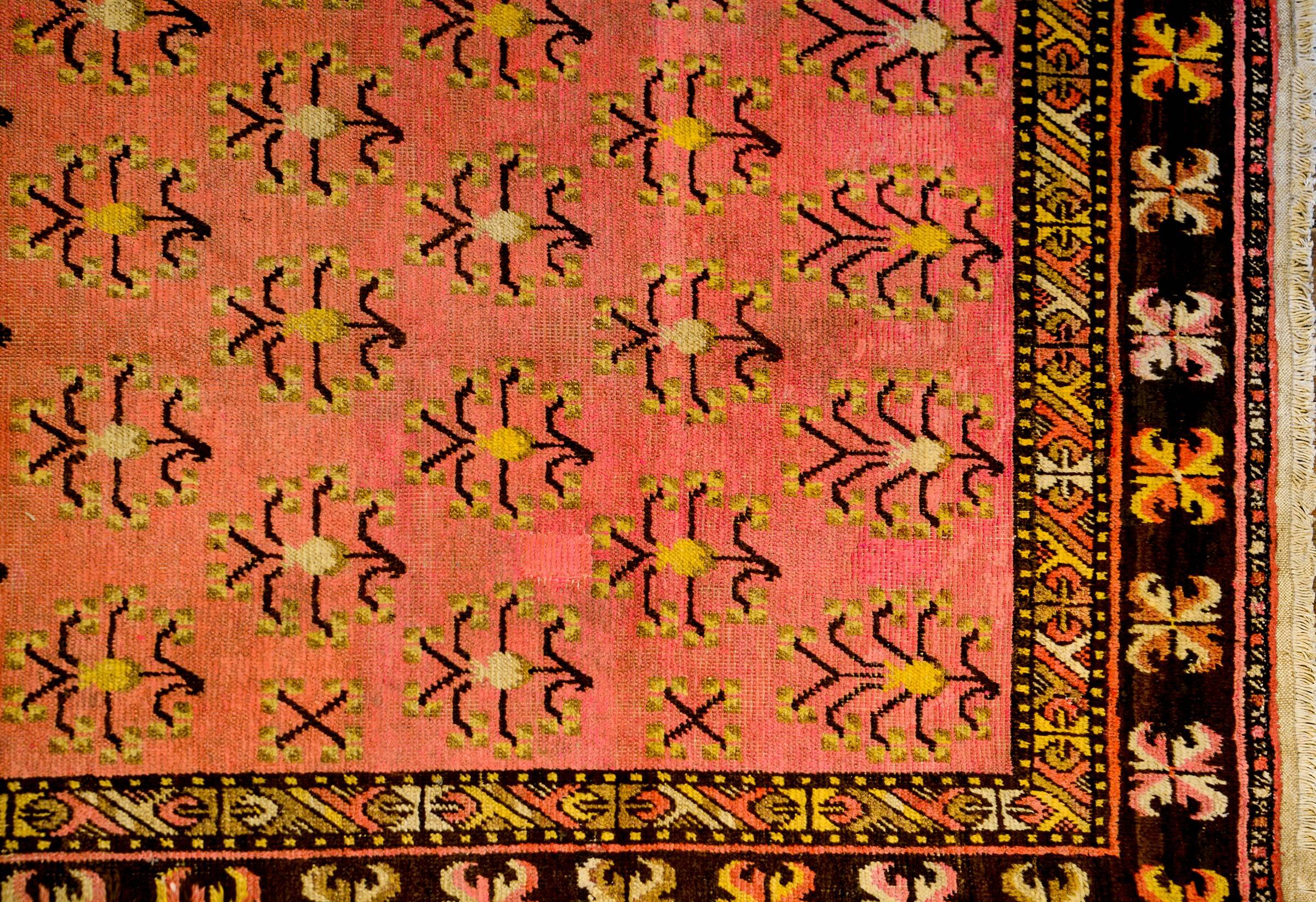 An unusual mid 20th century Central Asian Khotan rug with an interesting all-over tree-of-life pattern woven in gold and dark brown wool, on a fantastic pink background. The border is composed of four distinct patterns. The widest is a playful