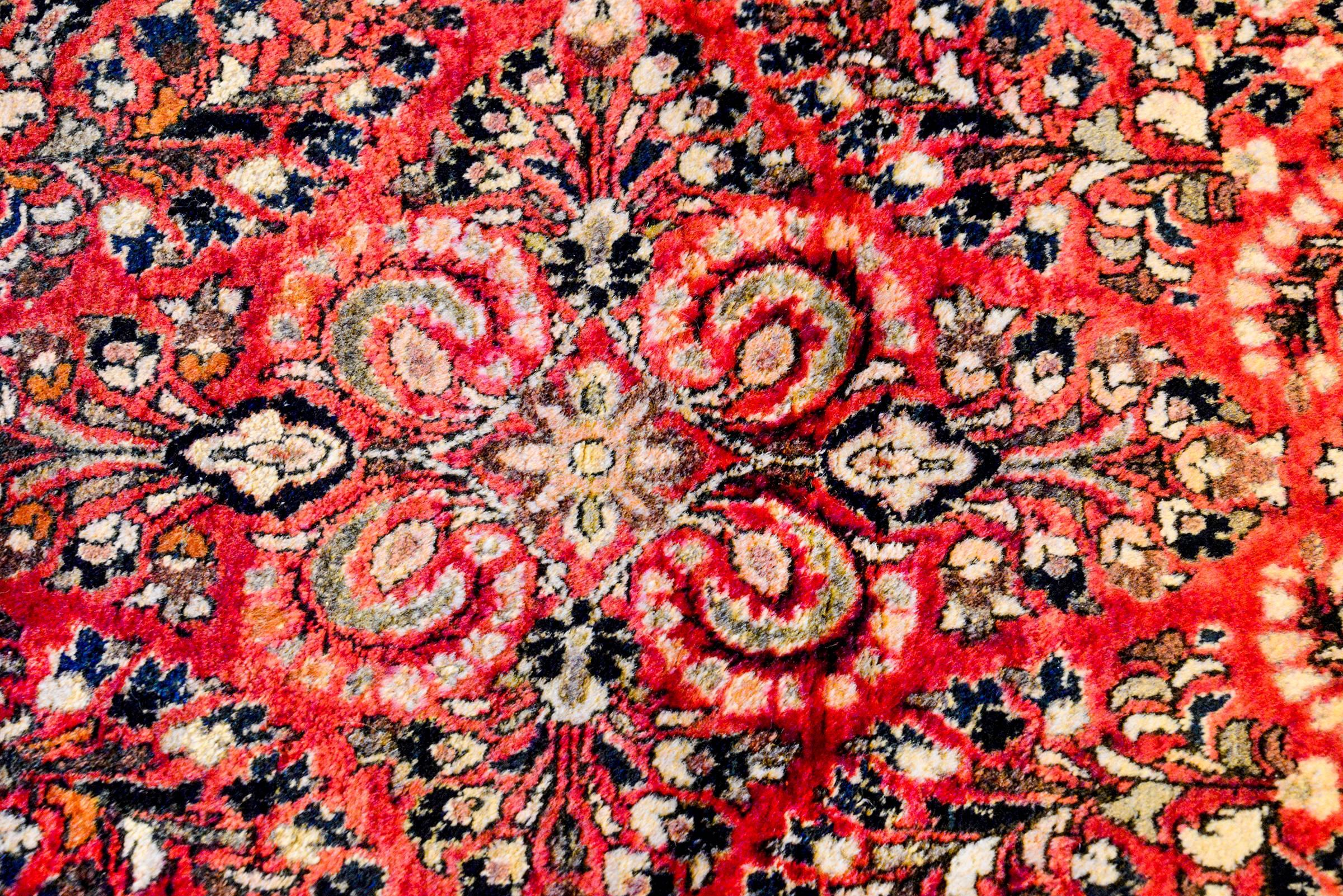 A beautiful early 20th century Persian Sarouk rug with a traditional all-over mirrored floral and vine tree-of-life pattern woven in light and dark indigo and cream colored wool, on a rich crimson background. The border is complex with a floral and