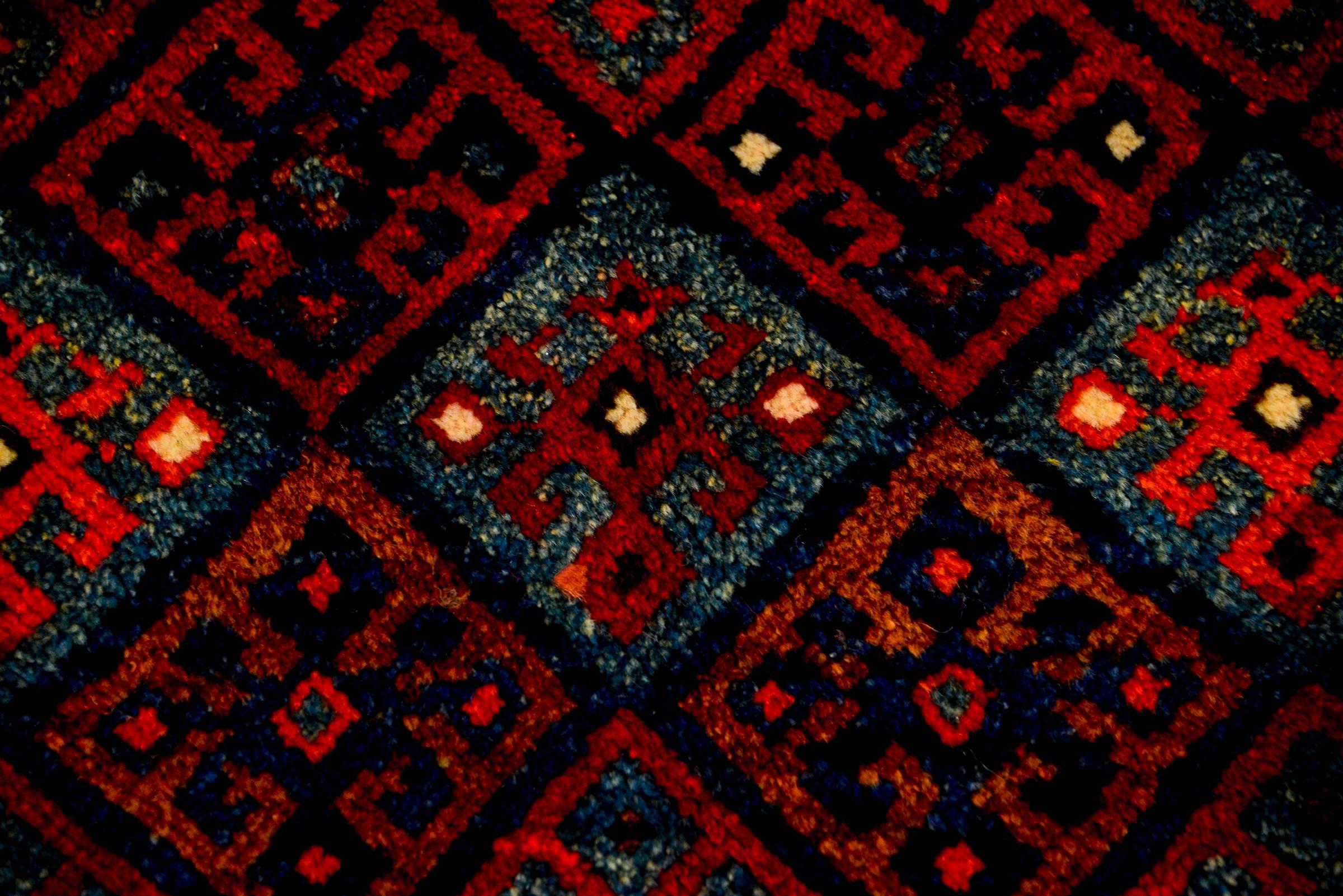 An early 20th century Persian Kurdish rug with a wonderful pattern containing multiple diamonds with geometric forms woven in crimson, light and dark indigo, cream, and copper colored wool. The border is complex, with two wide stripes, one with a