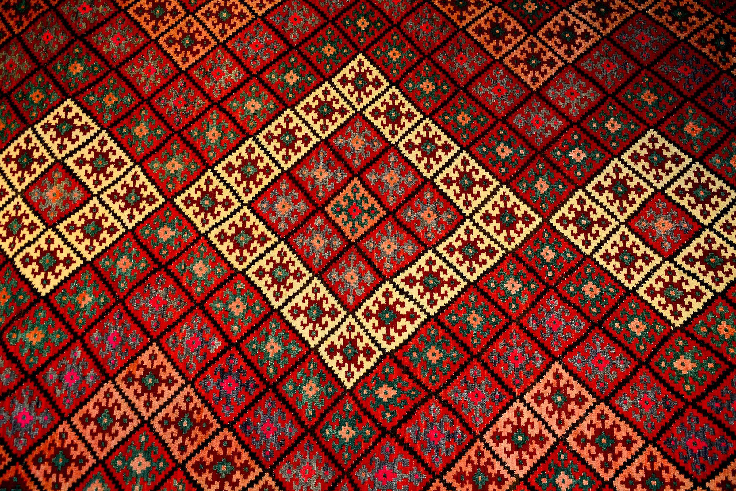 A mid-20h century Persian Saveh Kilim rug with a beautiful all-over diamond pattern of diamonds each with a geometric pattern, all woven in crimson, green, salmon, and grey vegetable dyed wool.