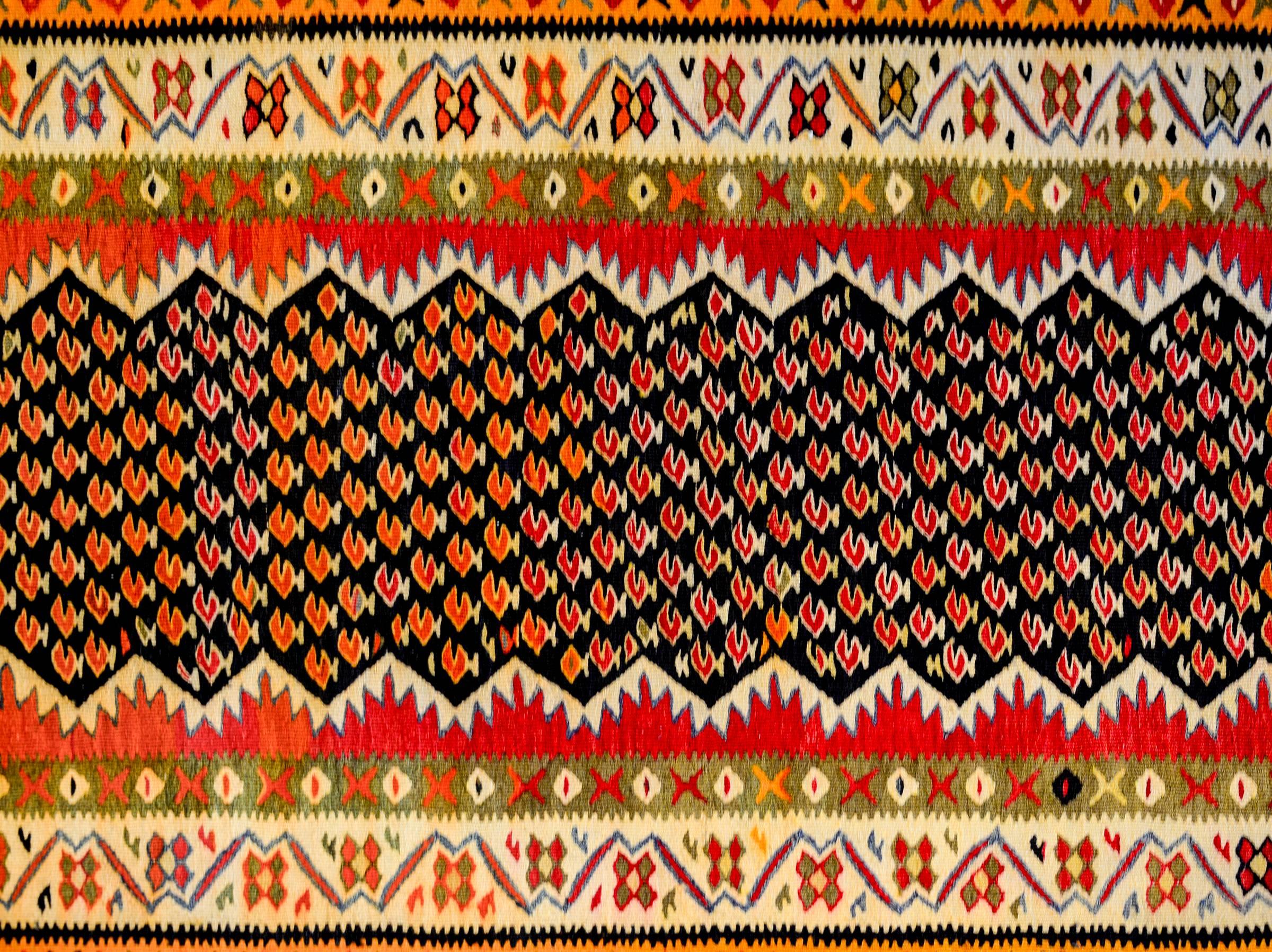A wonderful mid-20th century Persian Kurdish Kilim runner with an all-over crimson paisley pattern on a black background surrounded by a complex border of five distinct floral and geometric patterns, woven in crimson, green, gold, white, and black