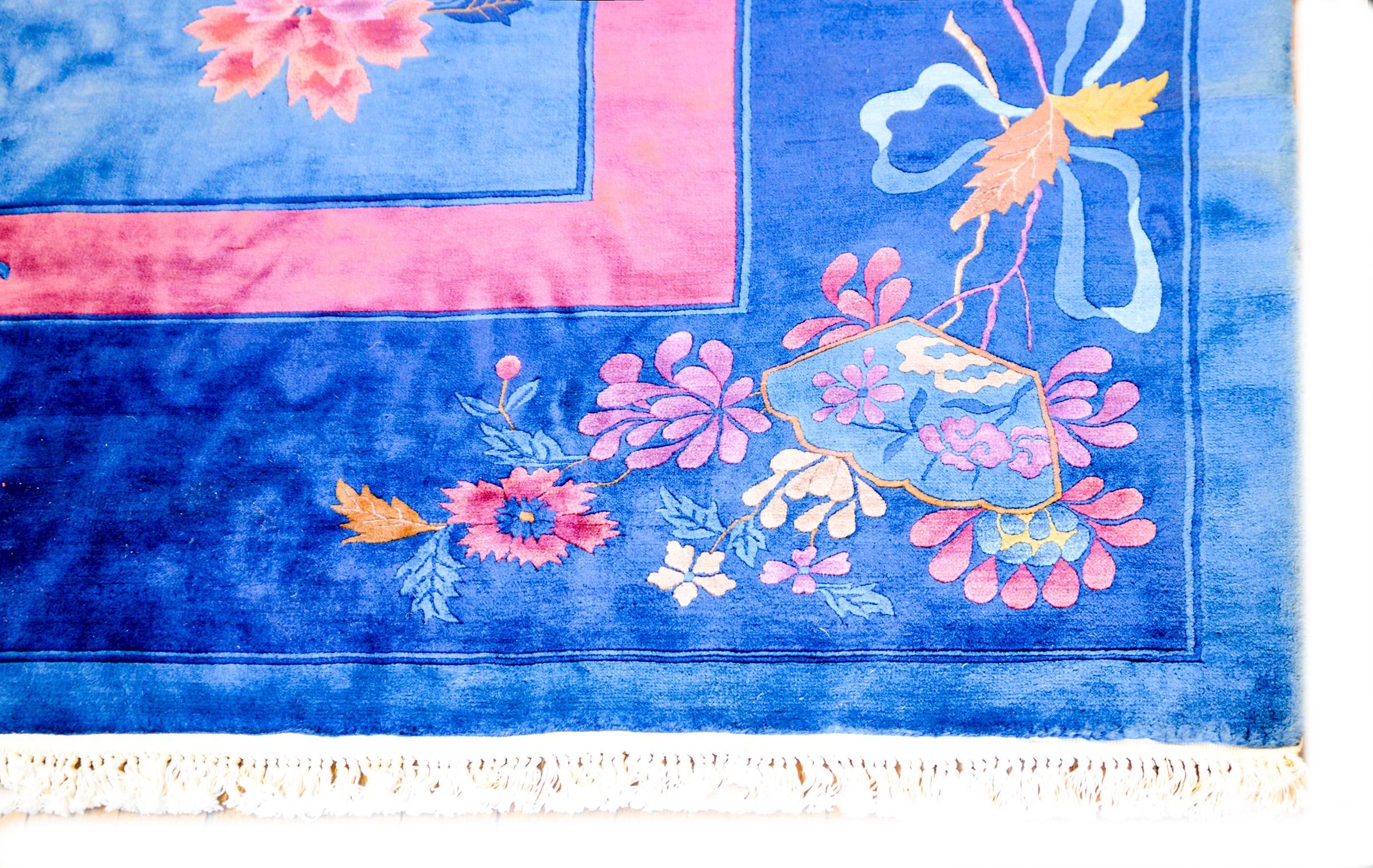 A wonderful early 20th century Chinese Art Deco rug with a brilliant light indigo field, surrounded by a thin coral colored stripe and a wide dark indigo border. The corners feature various auspicious longevity bestowing flowers like chrysanthemums,