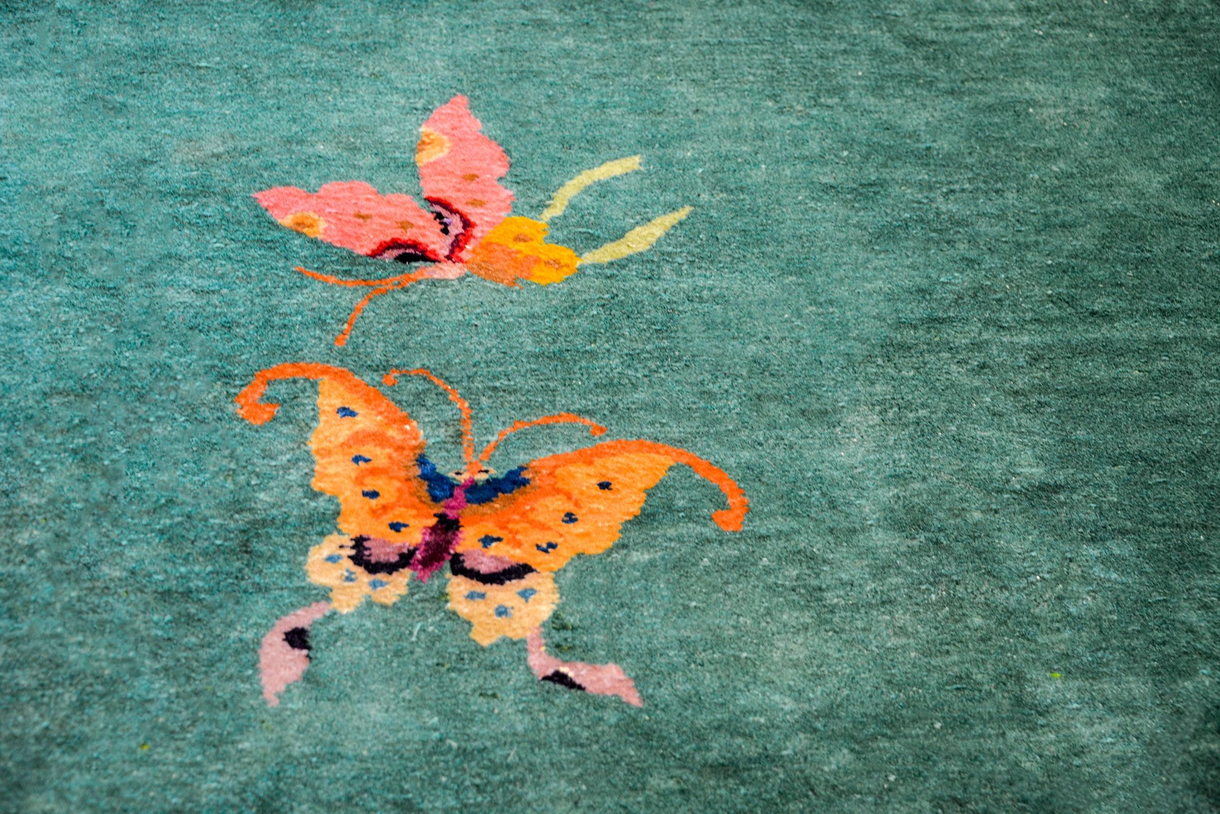 A brilliant Chinese Art Deco rug with a wonderful jade green field surrounded by a wide bright pink border with multiple multicolored auspicious peonies, chrysanthemum, and cherry blossoms, and two butterflies in the center.