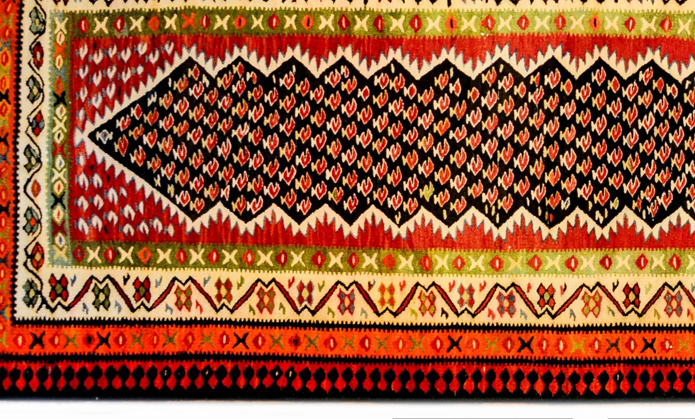 A wonderful mid-20th century Persian Kurdish Kilim runner with a beautiful crimson stylized paisley pattern on a black field surrounded by a wide multi-pattern border containing geometric and stylized floral patterns woven in crimson, green, indigo,
