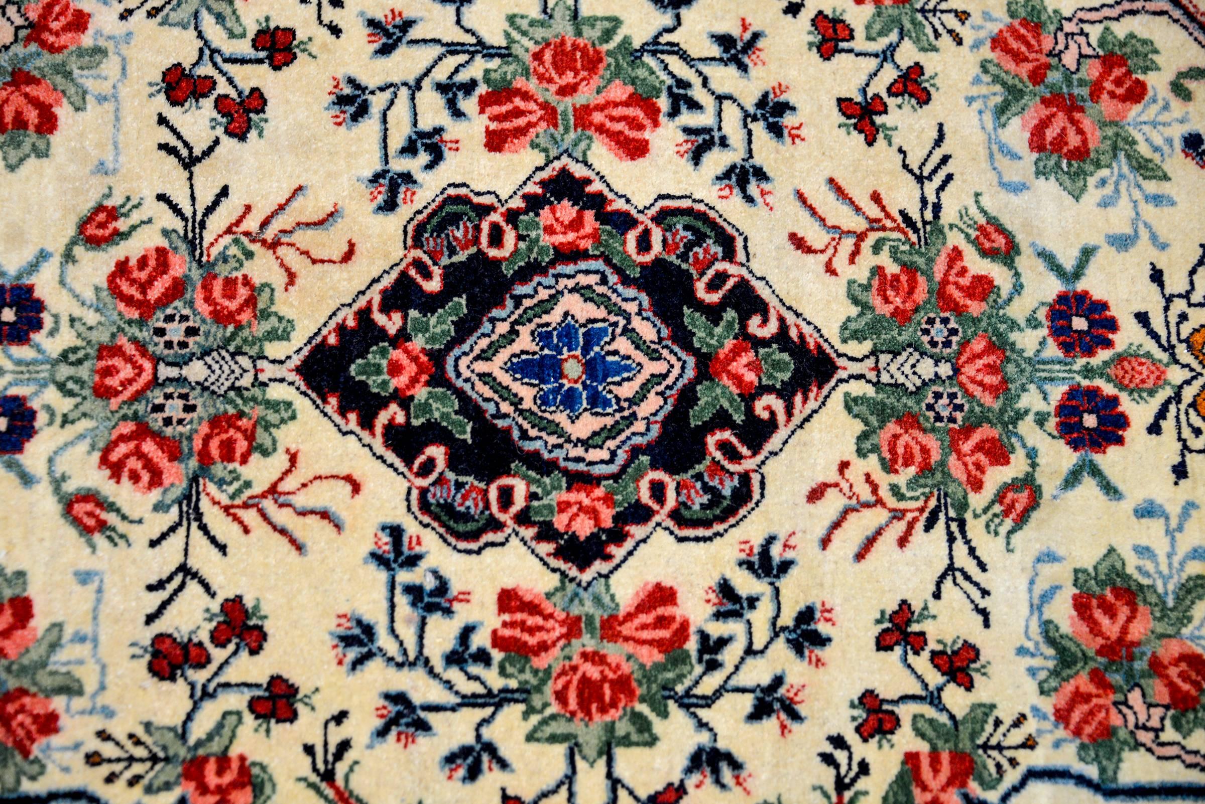 A sweet early 20th century petite Persian Bidjar rug with a beautiful floral pattern woven in red, indigo, green, and pink, on a cream colored background surrounded a by a complimentary border on a dark indigo background.