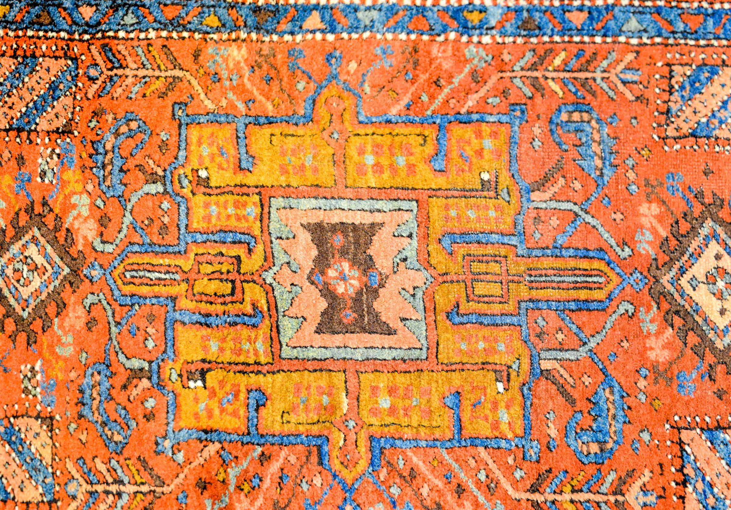A beautiful and brilliant Early 20th century Persian Heriz runner with multiple geometric and floral medallions woven in rich light and dark indigo, gold, green, and white vegetable dyed wool, on a bold orange background. The border is wide, with a