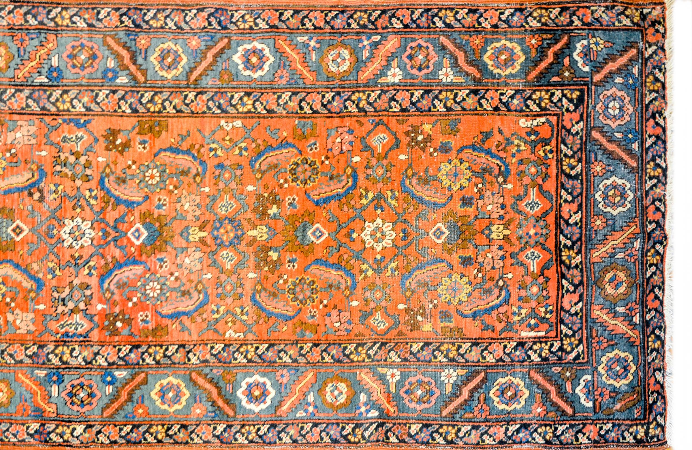 A beautiful and brilliant early 20th century Persian Heriz rug with an all-over floral pattern woven in rich light and dark indigo, gold, dark red and white vegetable dyed wool, on a bold coral background. The border is wide, with a beautiful floral