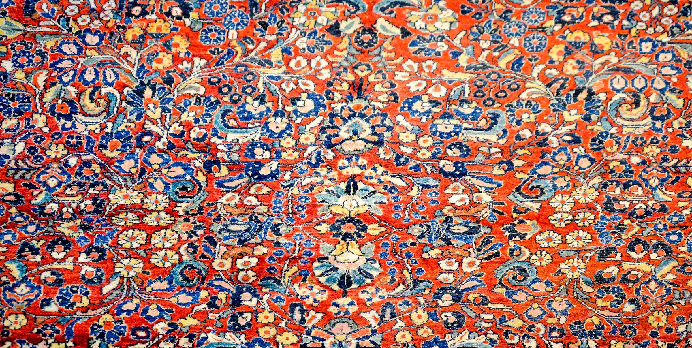 A wonderful early 20th century Persian Sarouk rug with a beautiful all-over mirror floral pattern woven in light and dark indigo, and natural wool, on an abrash cranberry background. The border is typical with a large-scale floral and vine pattern