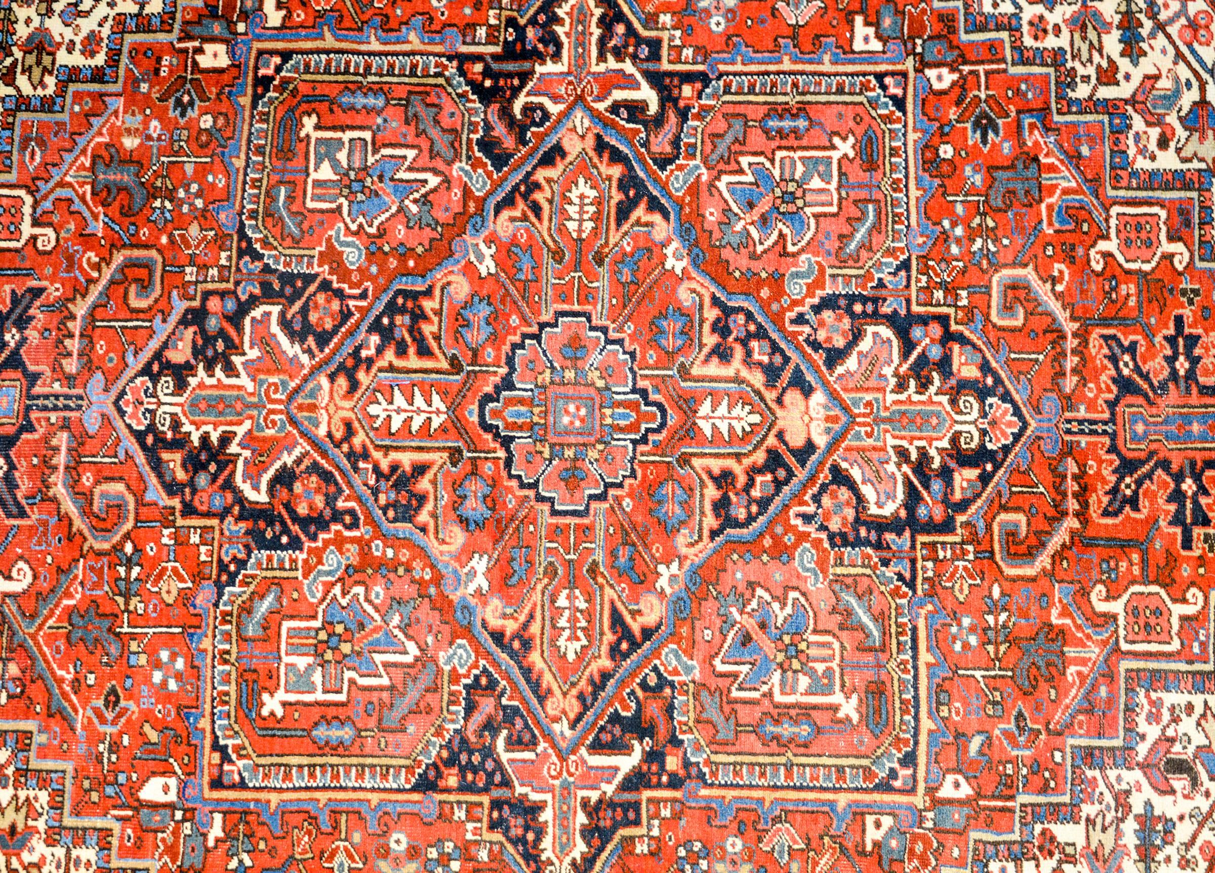 An amazing early 20th century Persian Heriz rug with a large central multi-lobed floral medallion with a crimson centre, surrounded by a deep indigo ring. The field is intensely woven with a complementary floral pattern. The border is comprised of a