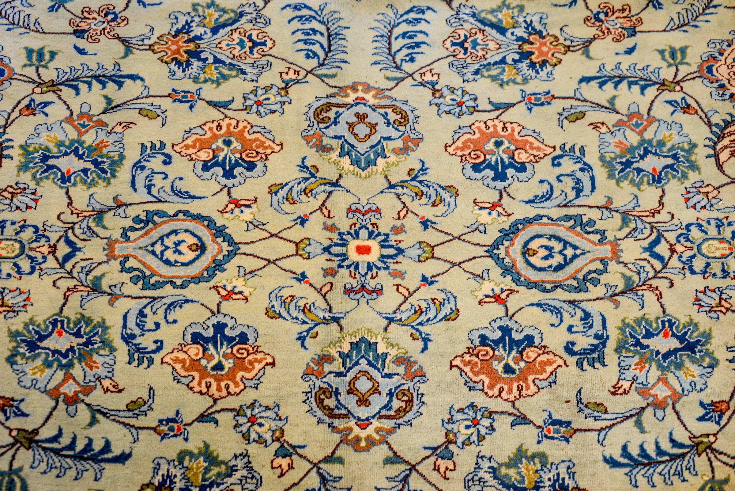 A fantastic early 20th century Persian Kashan rug with a sophisticated all-over pattern of flowering festoons woven in light and dark indigo, orange, green, and cream, on a beautiful natural undyed wool background. The border is complementary with a