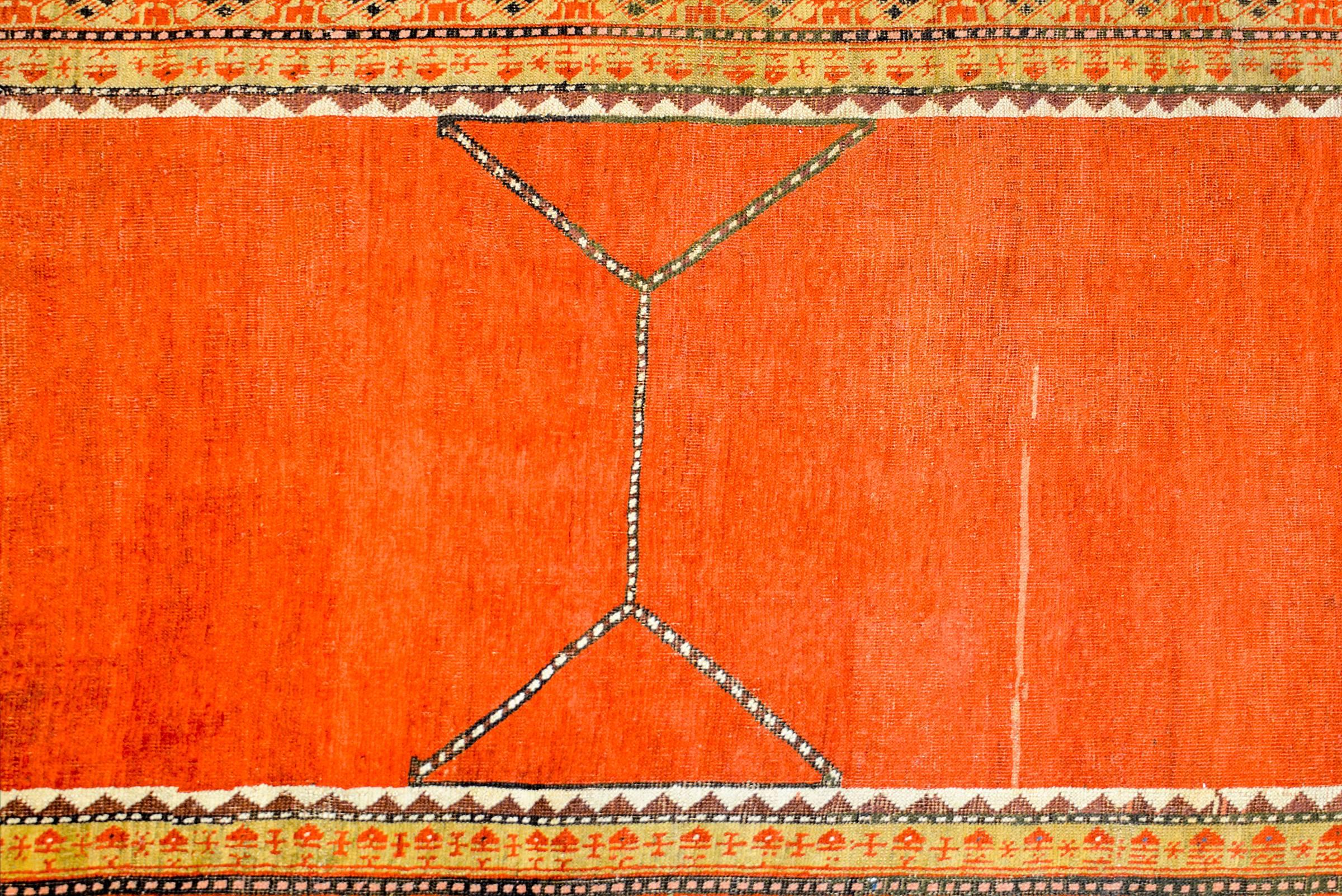 A stunning 1920s Turkish Konya rug with a bold abrash orange field with a simple line pattern across the centre, surrounded by a beautiful border of three stylized floral patterned stripes woven in pale green and crimson colors.