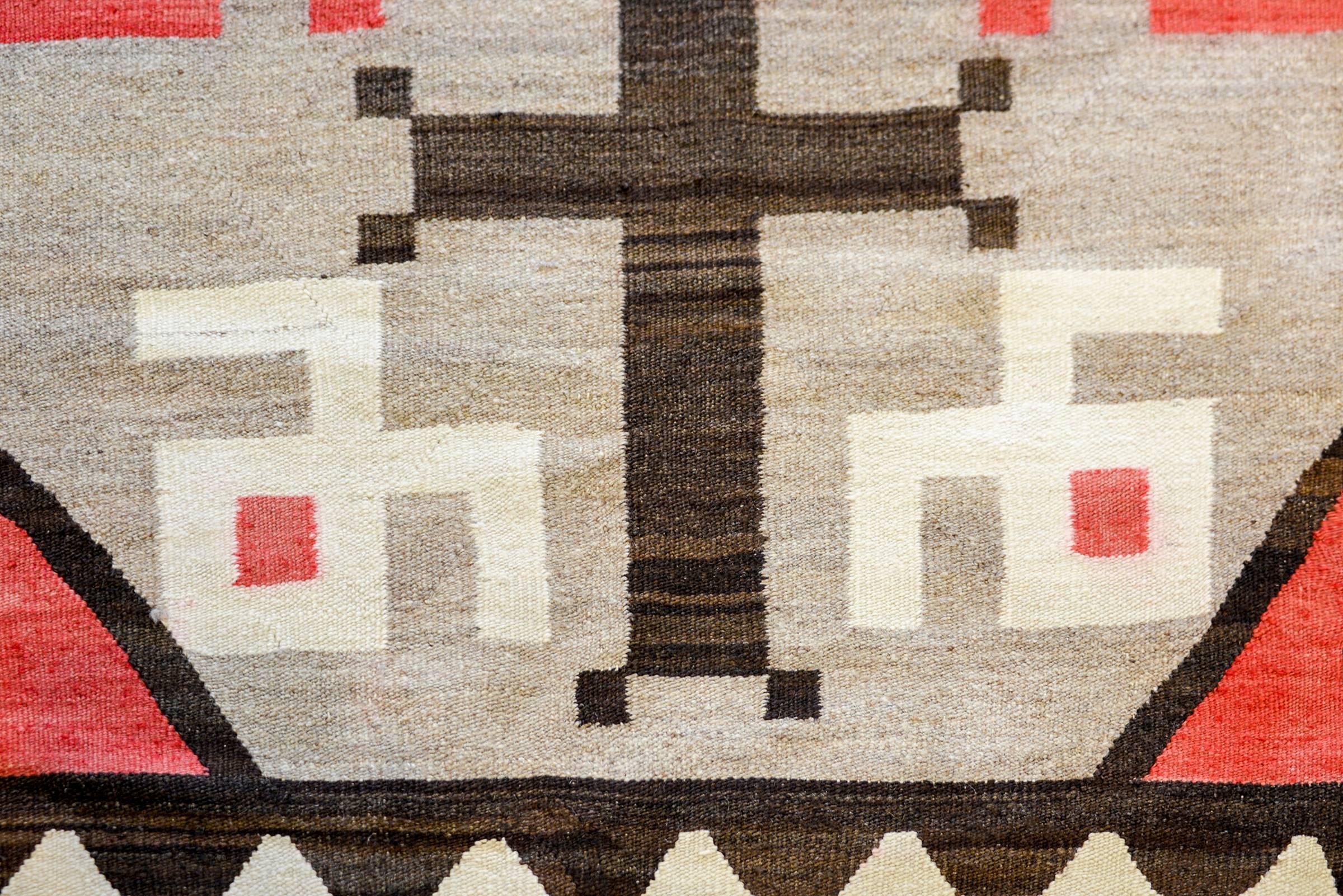 A striking mid-20th century Navajo rug with a bold pattern containing large-scale crosses amidst a field of red and white swirls on an brash grey background. The border is wide with a white zigzag stripe on a natural brown wool stripe with grey and