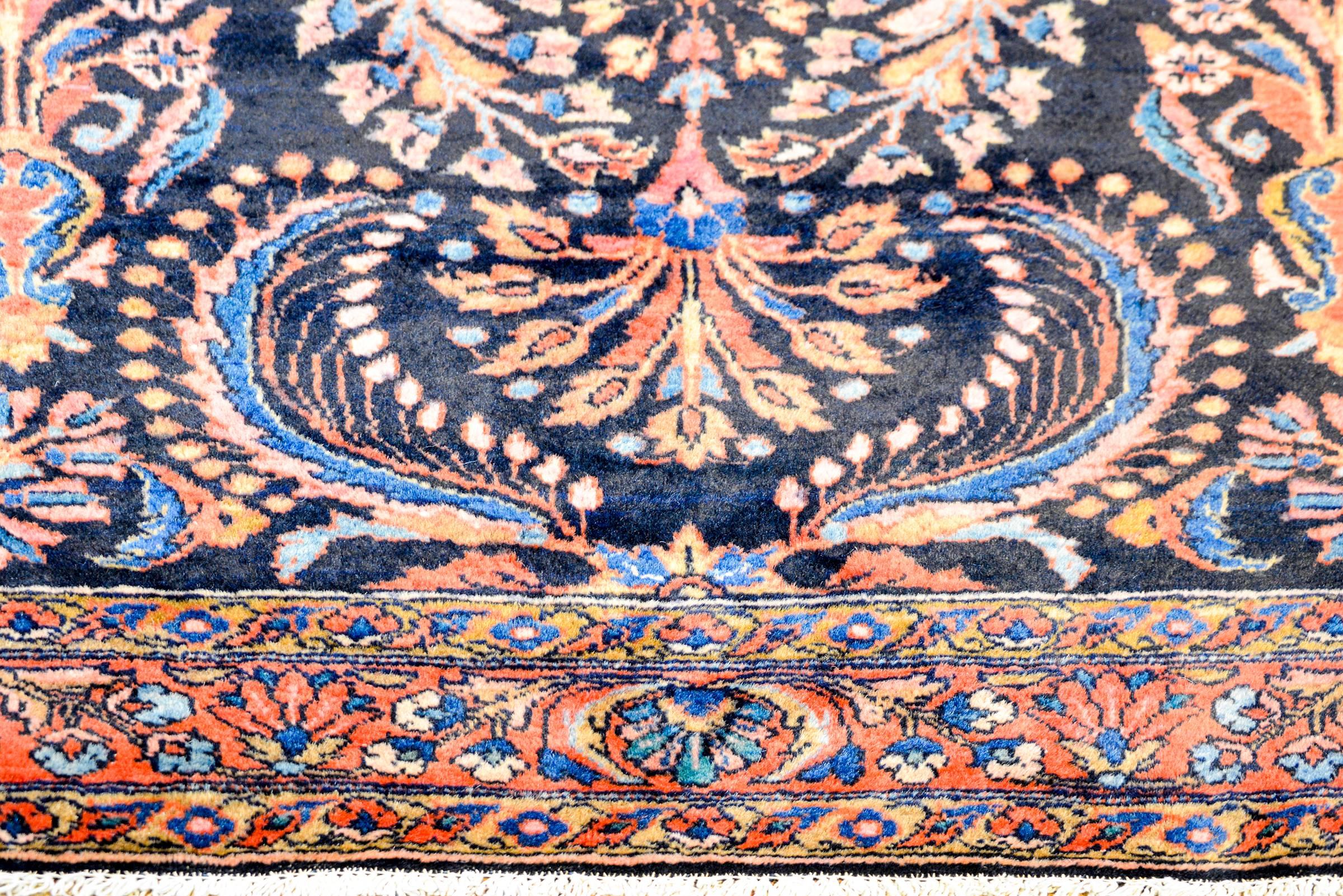 A gorgeous early 20th century Persian Lilihan rug with a dark indigo background, covered by a lacy, multicolored large-scale scrolling leaf and floral pattern woven light and dark indigo, crimson, pink, and natural undyed wool, surrounded by a wide