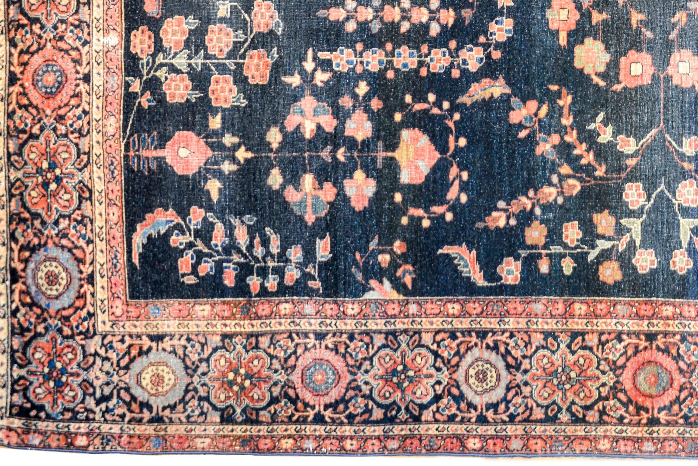 A wonderful and classic early 20th century Persian Sarouk Farahan rug with a traditional mirrored floral pattern woven in crimson, pink, and light indigo, on a dark indigo background. The border is contrasting with a wide densely woven floral and