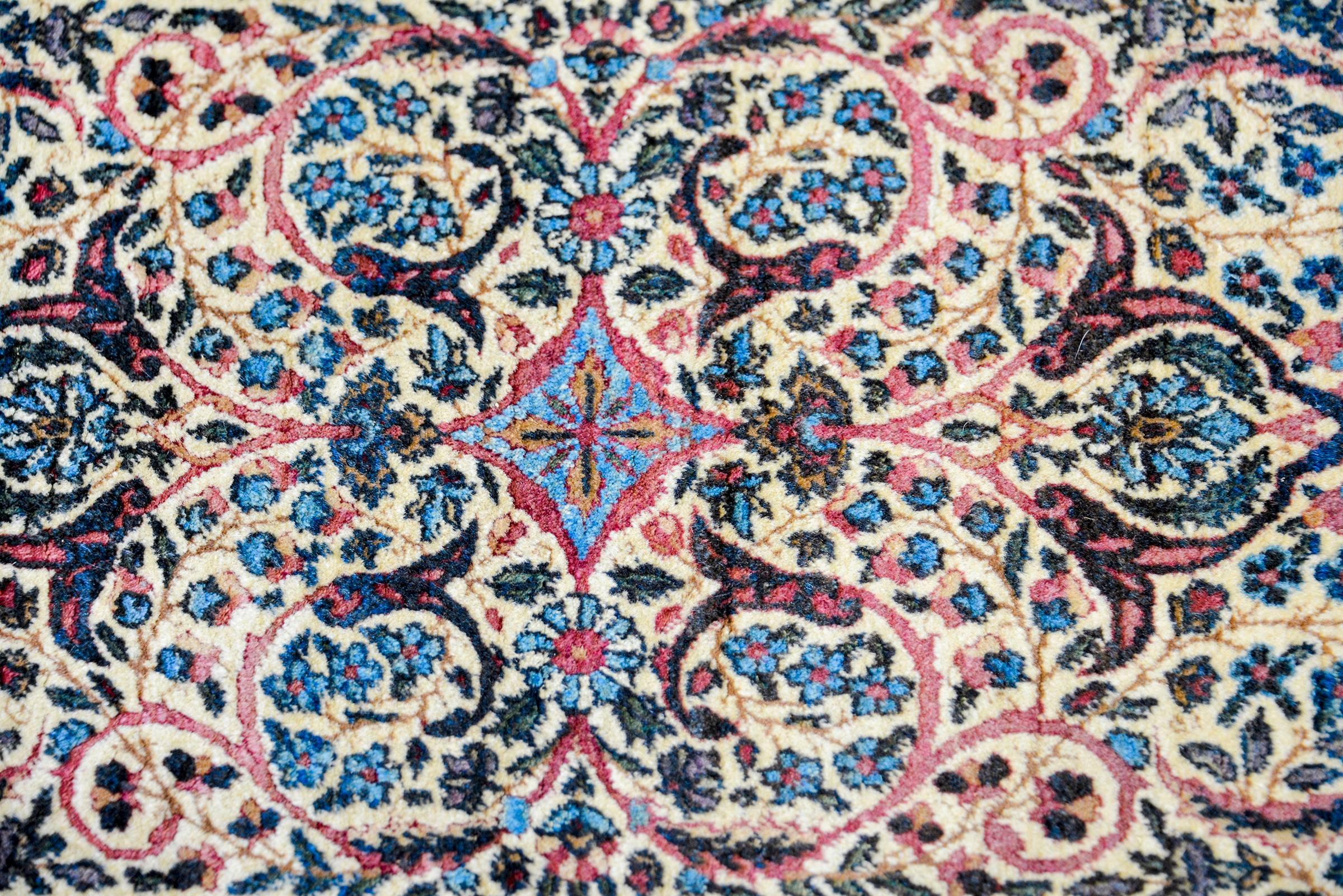 Un meraviglioso tappeto persiano Kirman dell'inizio del XX secolo con un motivo floreale e di foglie a specchio densamente intrecciato in lana tinta al vegetale color indaco, rosa, oro e verde. Il bordo è ampio e presenta molteplici motivi floreali,
