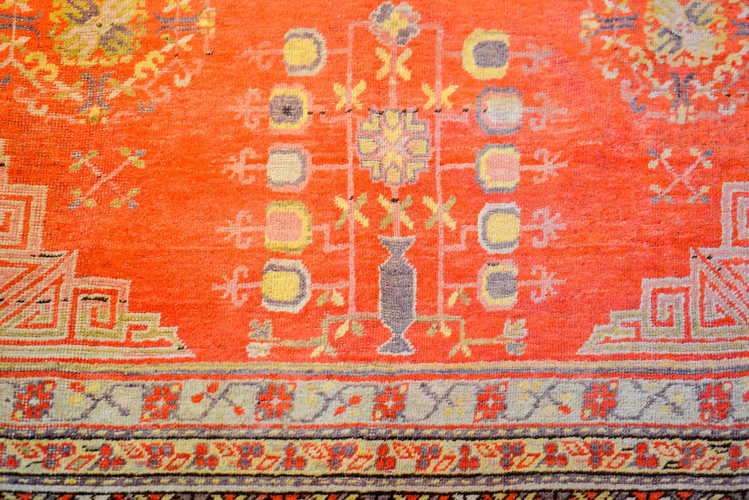 An early 20th century Central Asian Khotan rug with a beautiful orange field of pomegranate, trees-of-life, and floral patterns. The border is wonderfully rendered consisting of a Buddhist meandering motif pattern, multiple petite floral and vine