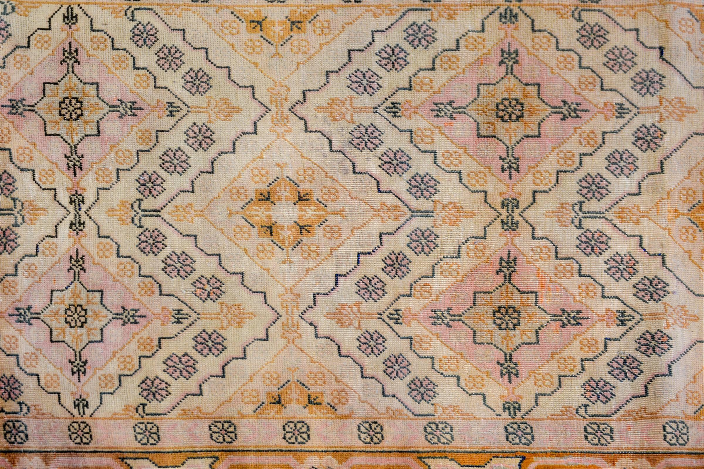 A wonderful early 20th century Central Asian Khotan rug with a beautiful all-over pattern with alternating diamonds and flowers creating a great zigzag pattern across the field, woven in pink, gold, natural undyed wool, and outlined in black. The