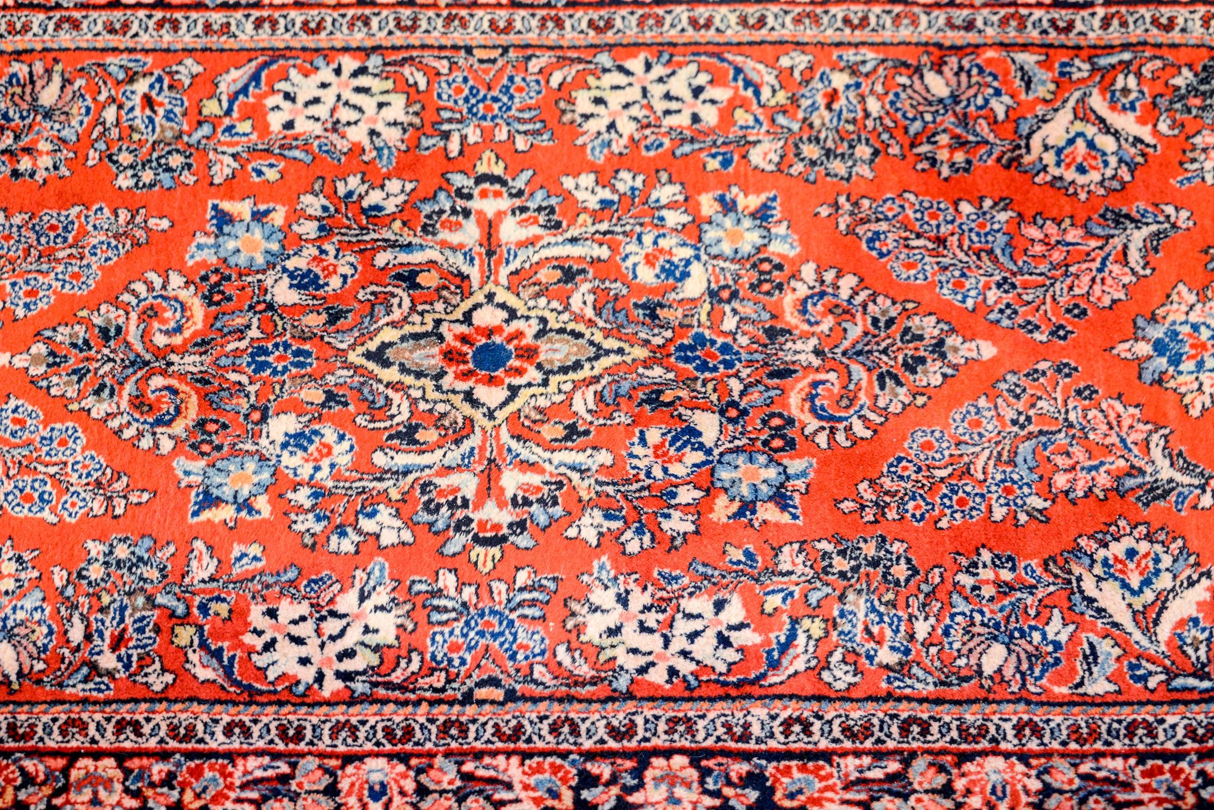 A beautiful early 20th century Persian Sarouk rug with a beautiful mirrored floral pattern woven in light and dark indigo, pink, brown, on a rich crimson background. The border is wonderfully rendered with a floral and vine pattern on an indigo