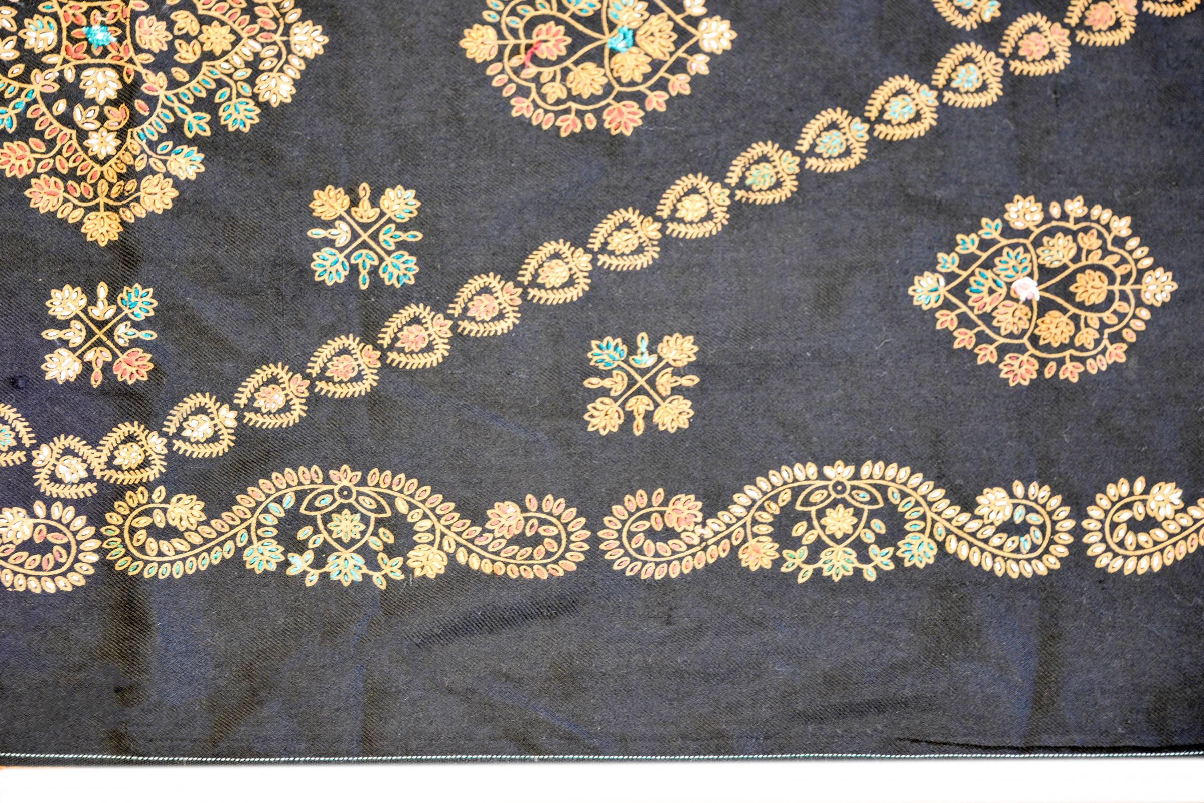 An expertly embroidered late 20th century Indian Suzani textile with green, gold, pink, and blue silk thread comprising a diamond form with stylized flowers across the black cotton ground.