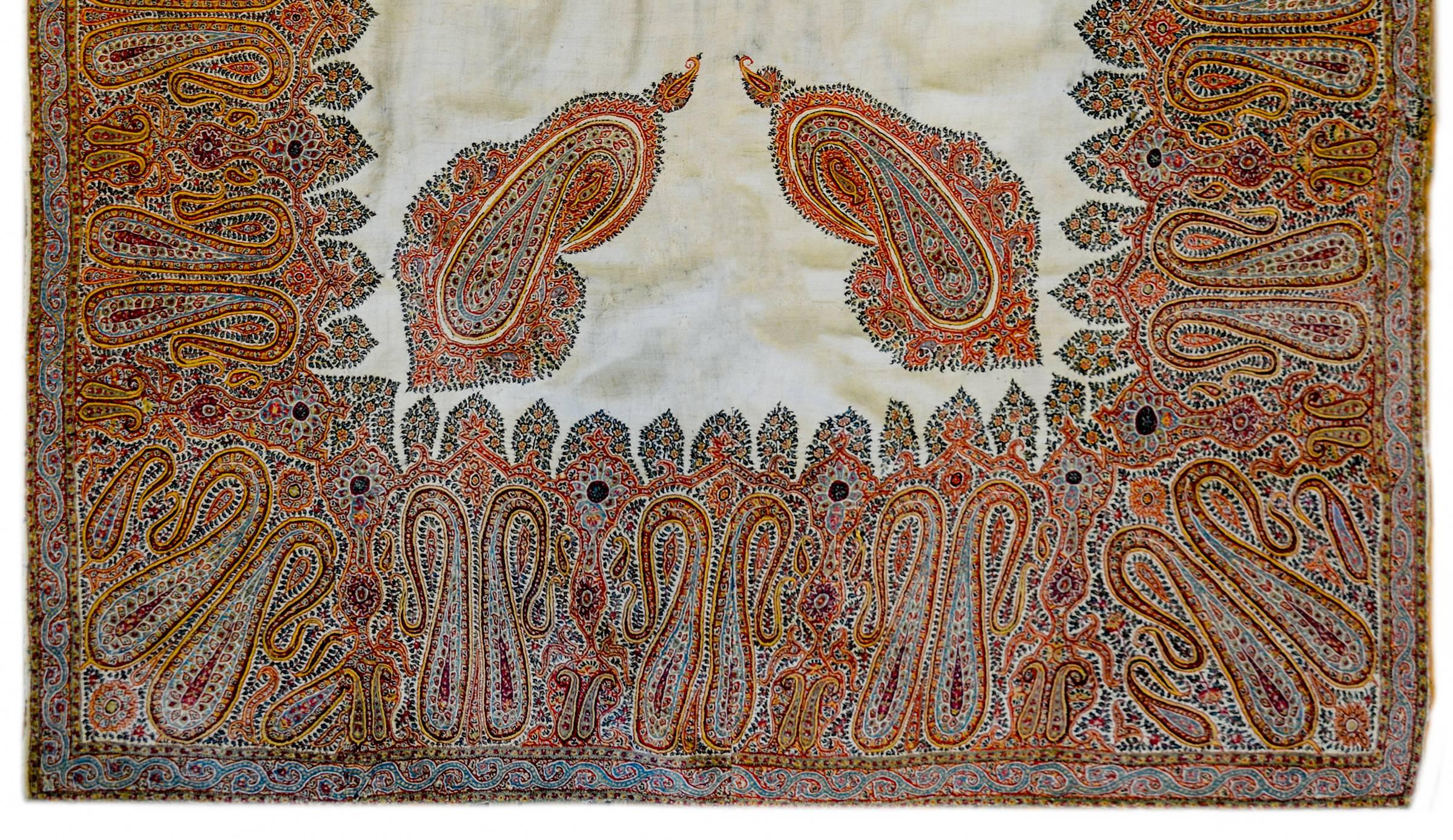 An unbelievable early 20th century Kirman silk embroidered Suzani textile with a beautiful pattern of densely embroidered paisley pattern woven in myriad colors of silk thread surrounding a relatively empty field containing four large paisley shapes.