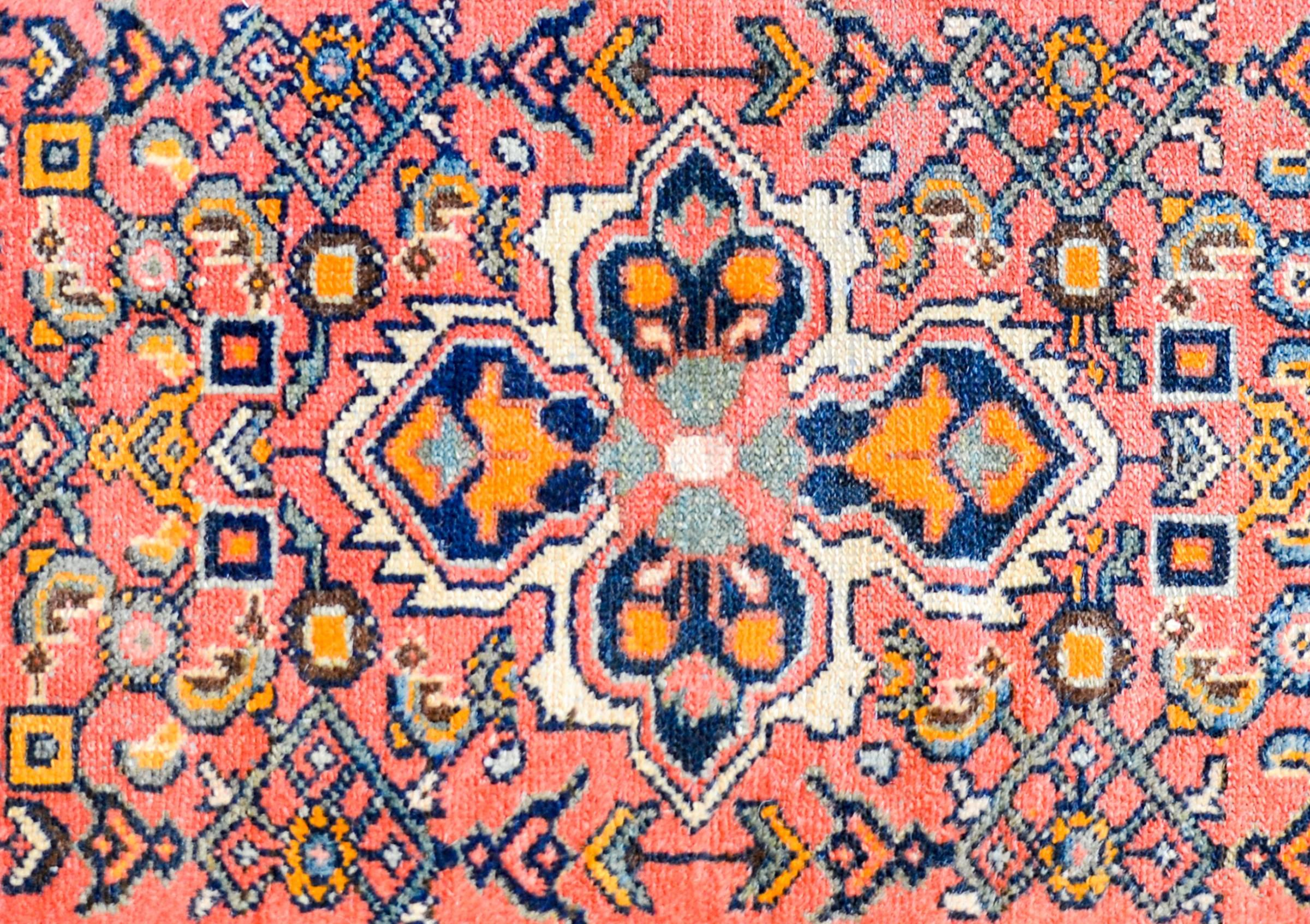 A wonderful mid-20th century Persian Hamadan rug with a four-lobed floral medallion woven in indigo, orange, pale green, and white amidst a field of flowers and trellis designs on a pale pink background. The border is complex with a large-scale