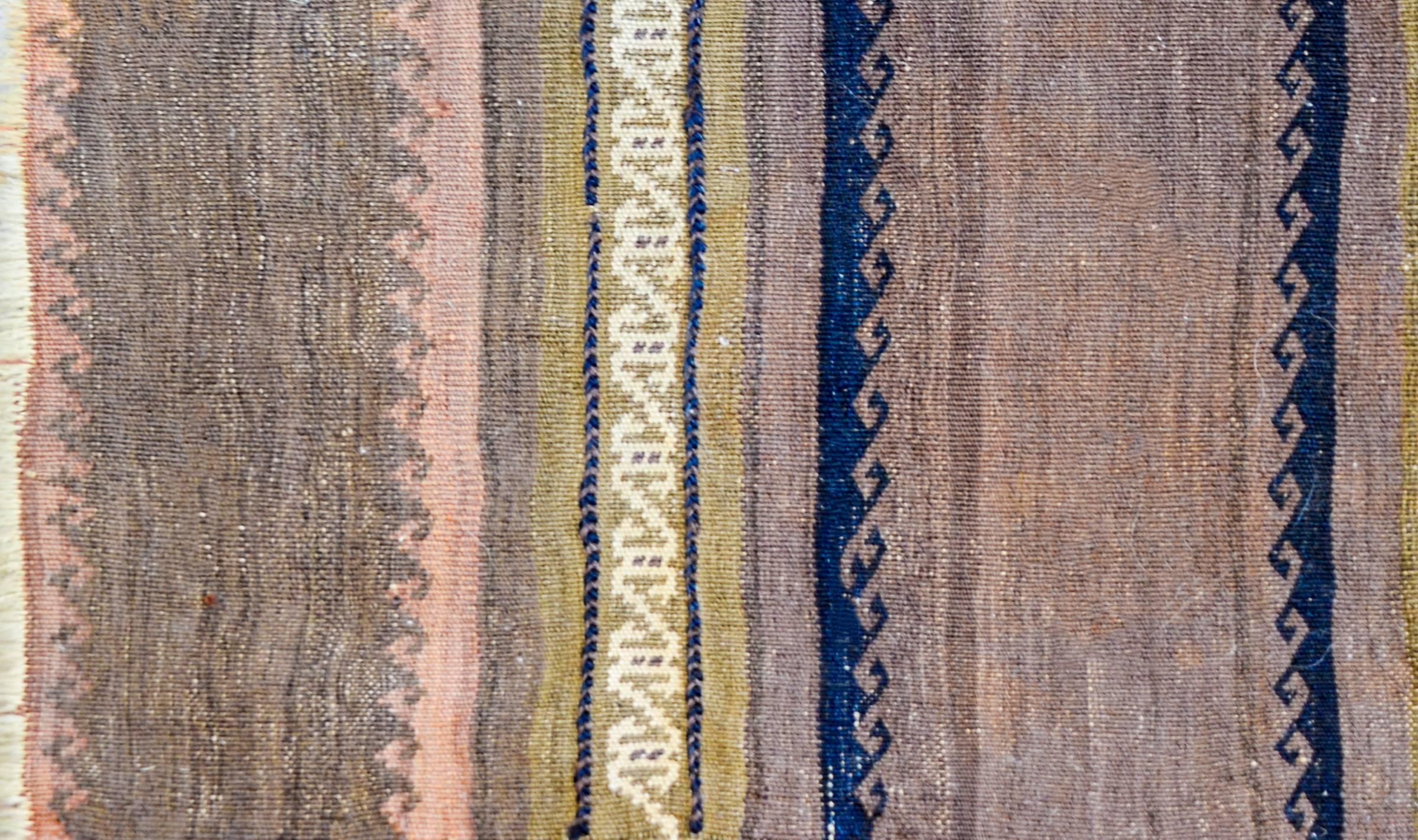 A beautiful petite early 20th century Baluch Kilim rug with a pretty pattern of pink, indigo, and pale green stripes, some with a wave pattern, and others with a stylized floral motif. The background is chic, with an abrash natural undyed brown wool