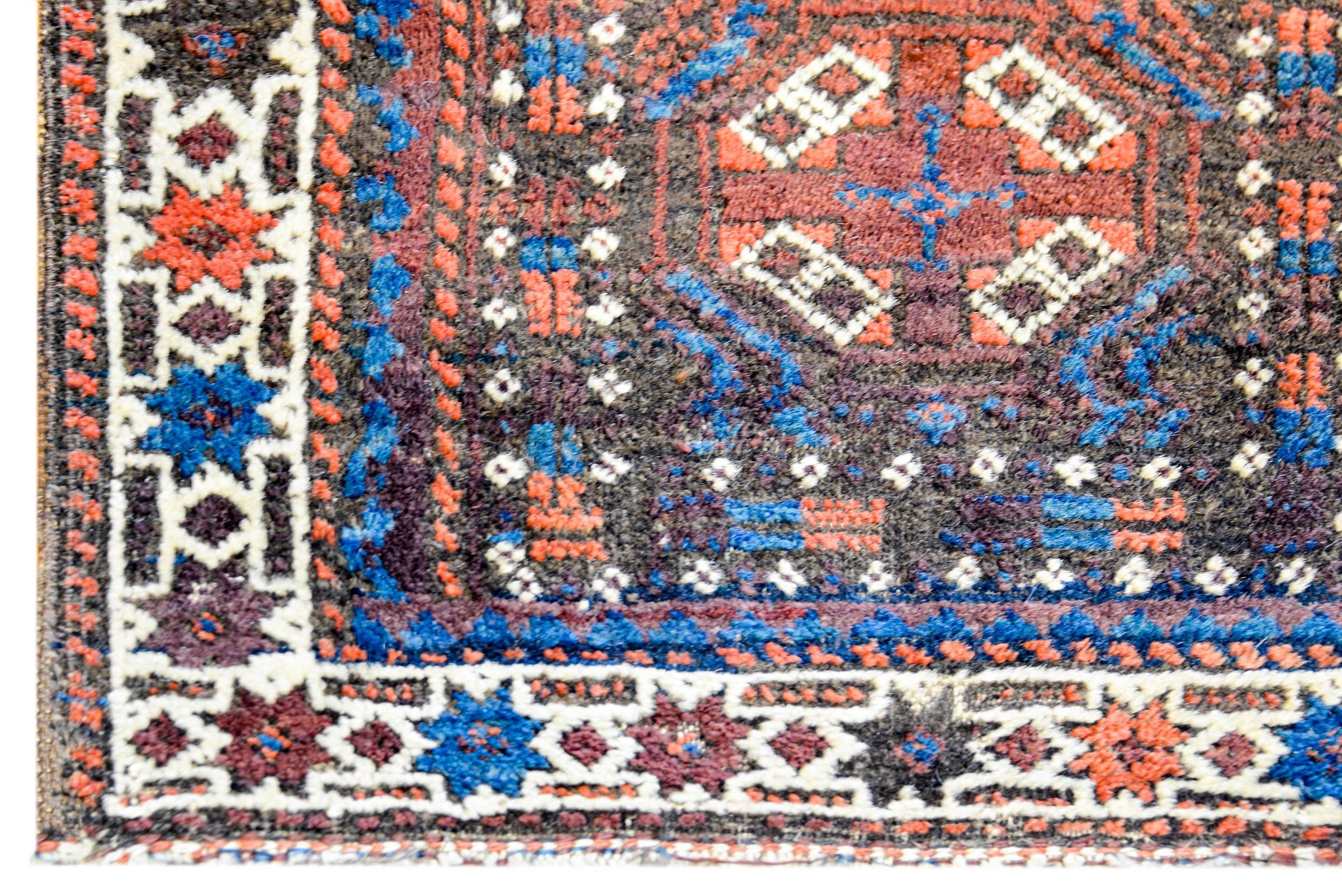 A beautiful early 20th century Persian Turkmen rug composed with two squares each with its own medallion amidst fields of stylized flowers, surrounded by matching stylized flower borders, all woven in indigo, crimson, and orange vegetable dyed wool