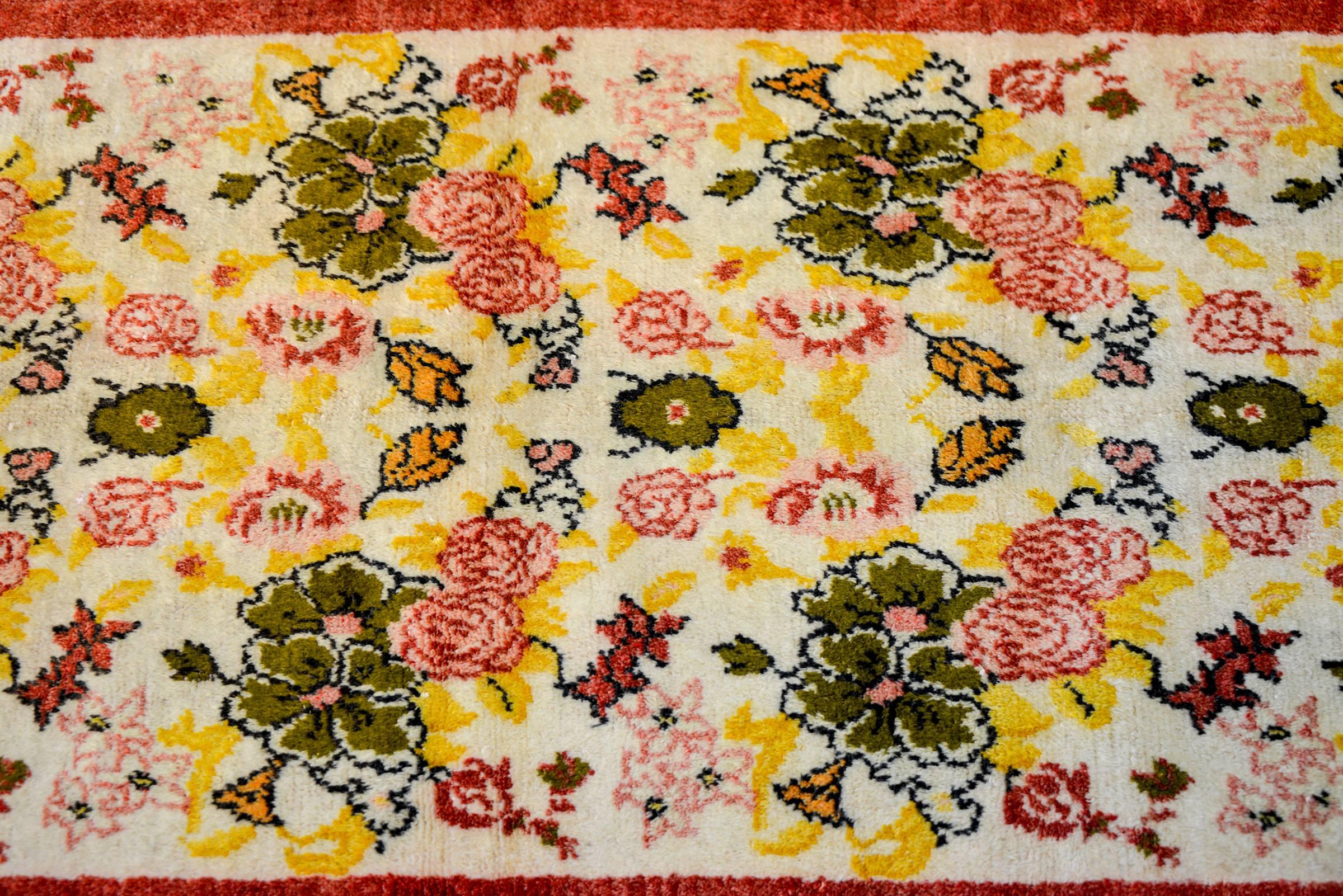 A unique early 20th century Turkish rug with a repeated pattern of large green and small rose colored flowers, with gold and orange leaves, on a white background. The border is simple with a cranberry band.