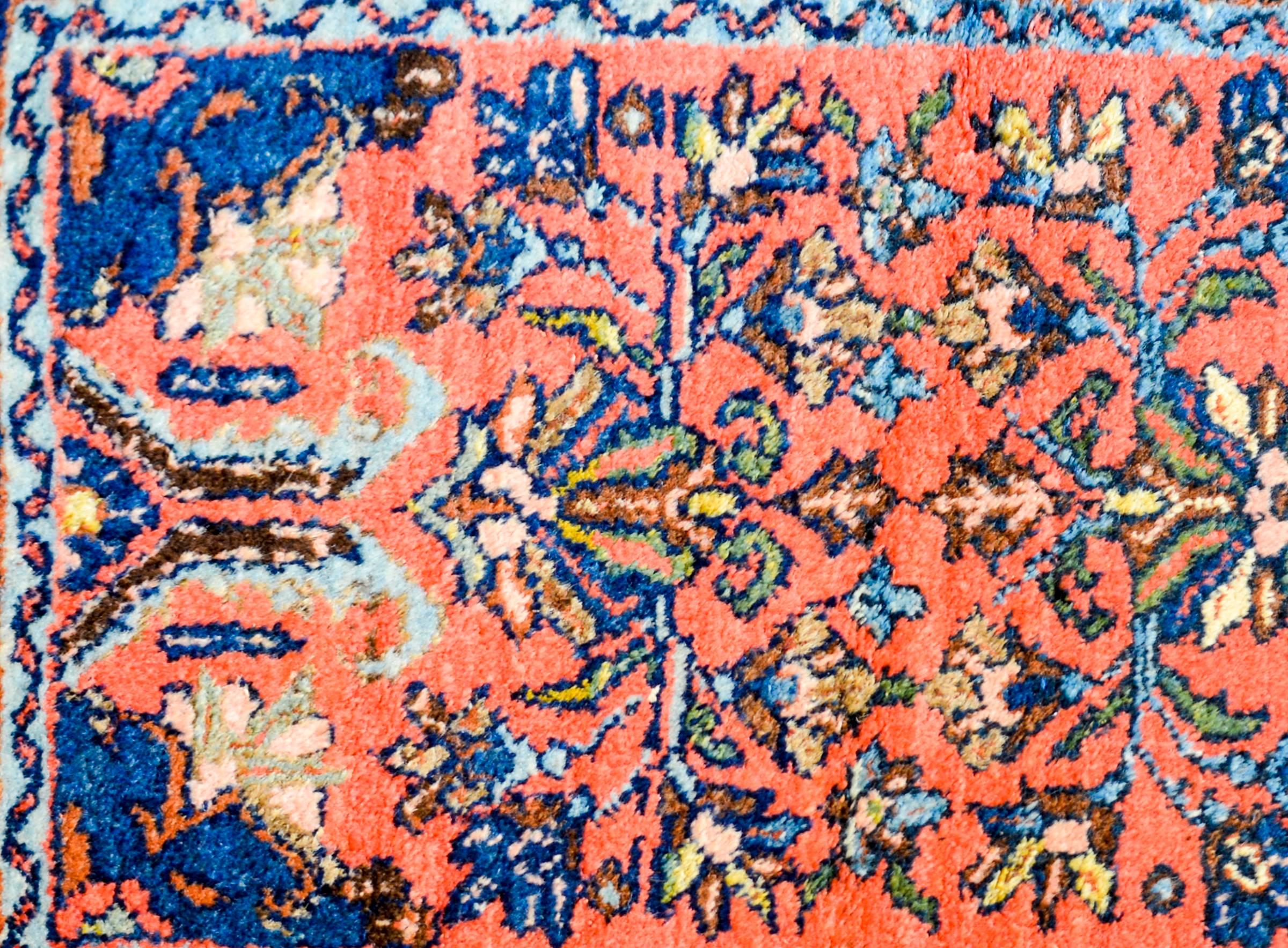 A wonderful mid-20th century Persian Hamadan rug with a mirrored floral pattern woven in indigo, orange, pale green, and white on an abrash coral wool background. The border is complex with a large-scale stylized floral pattern flanked by two