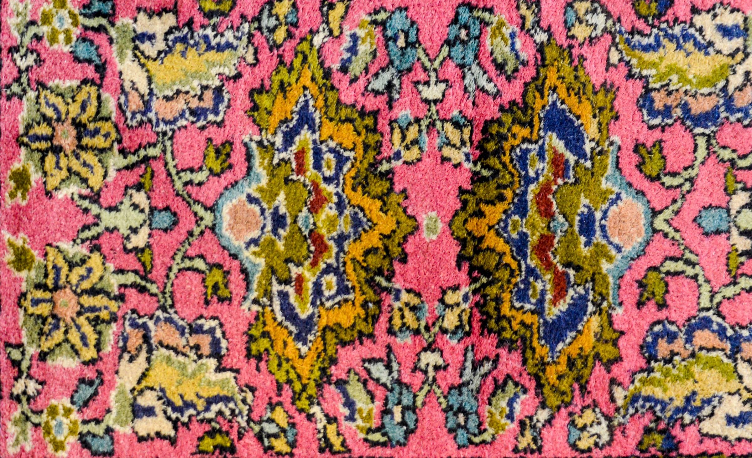 An early 20th century Indian Agra rug with a wonderful large-scale mirrored floral and vine pattern woven in light and dark green, gold, and indigo on a bright pink background, surrounded by a thin floral and leaf border.