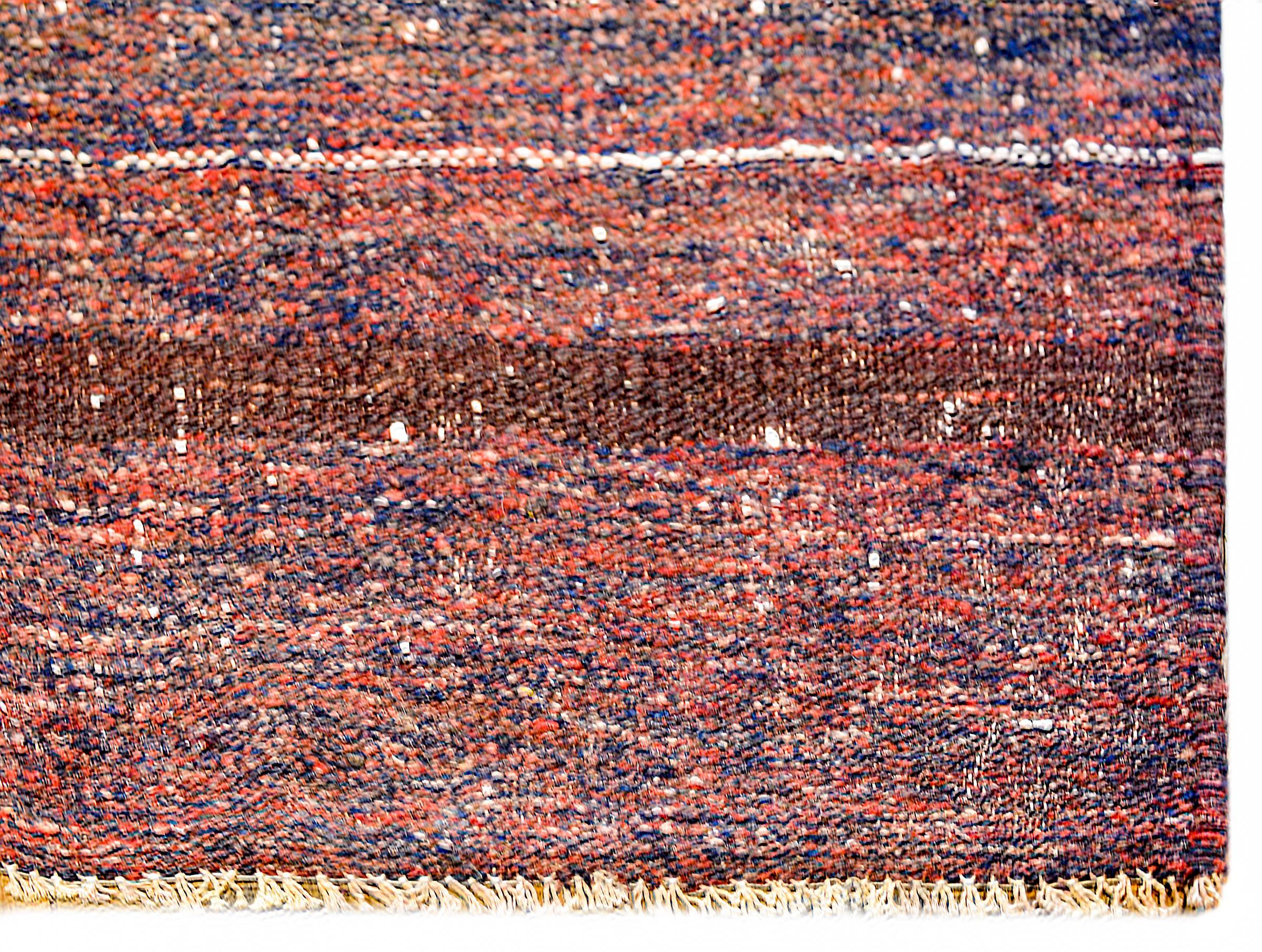 A brilliant vintage Persian Gabbeh Kilim rug woven in crimson and indigo wool with a wonderful stylized flower and simple whip stitched edge trim.
