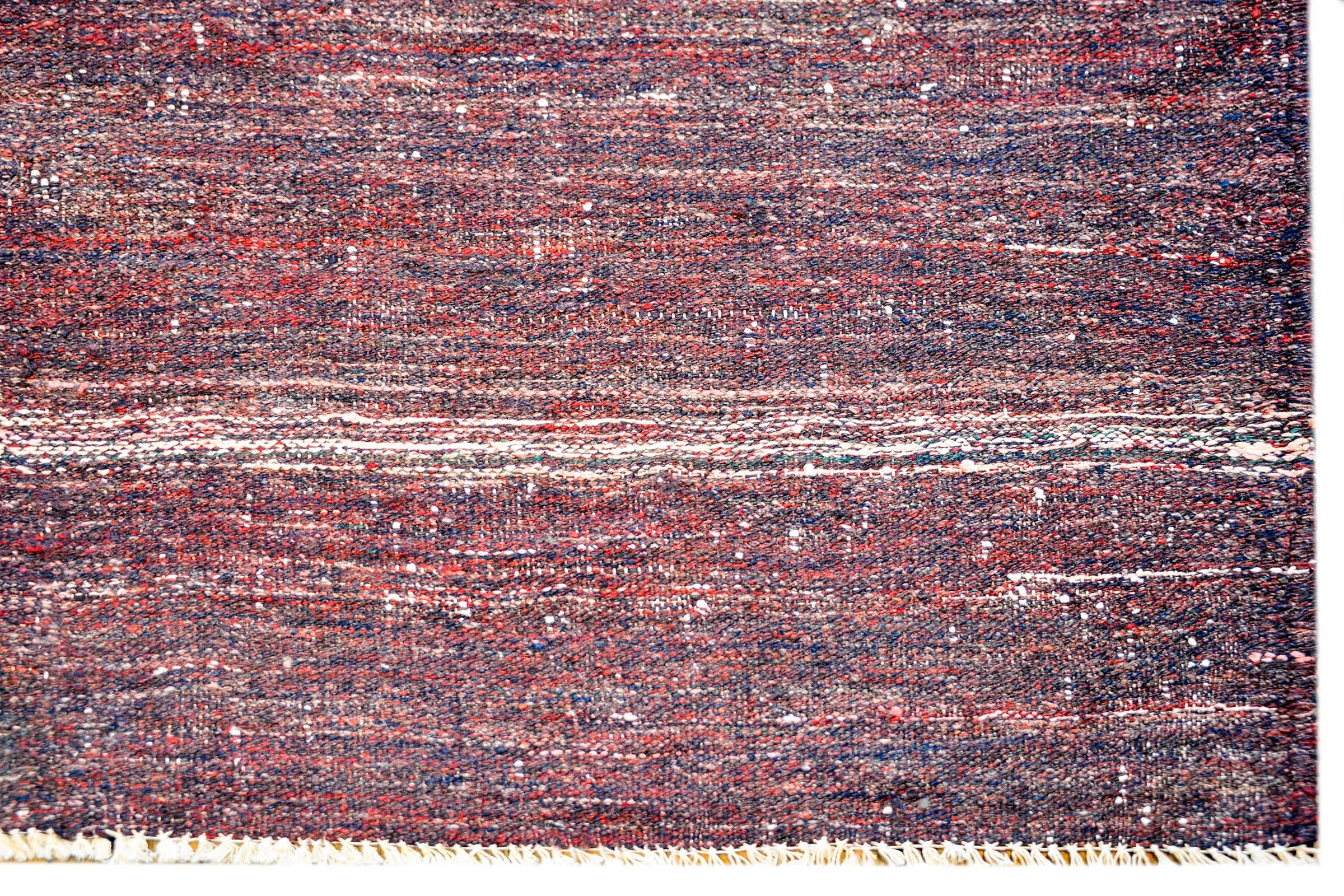 A brilliant vintage Persian Gabbeh Kilim rug woven in crimson and indigo wool with a wonderful stylized flower and simple whipstitched edge trim.