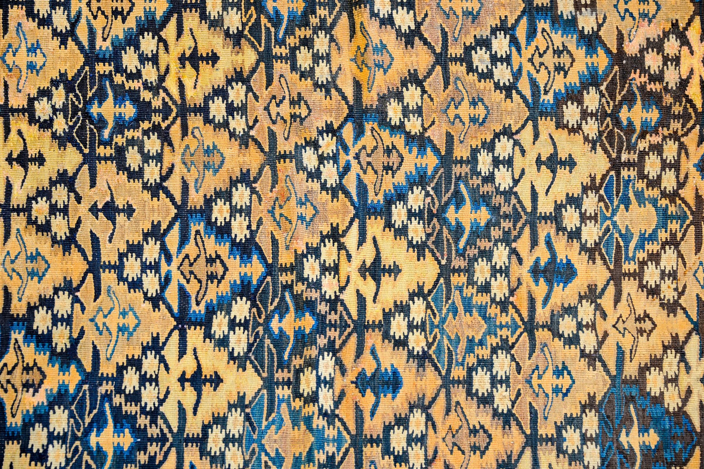 A wonderful early 20th century Persian Qazvin Kilim rug with an all-over tree-of-life pattern woven in indigo, green, gold, and natural undyed wools. The border is complex, woven with multiple geometric designs.