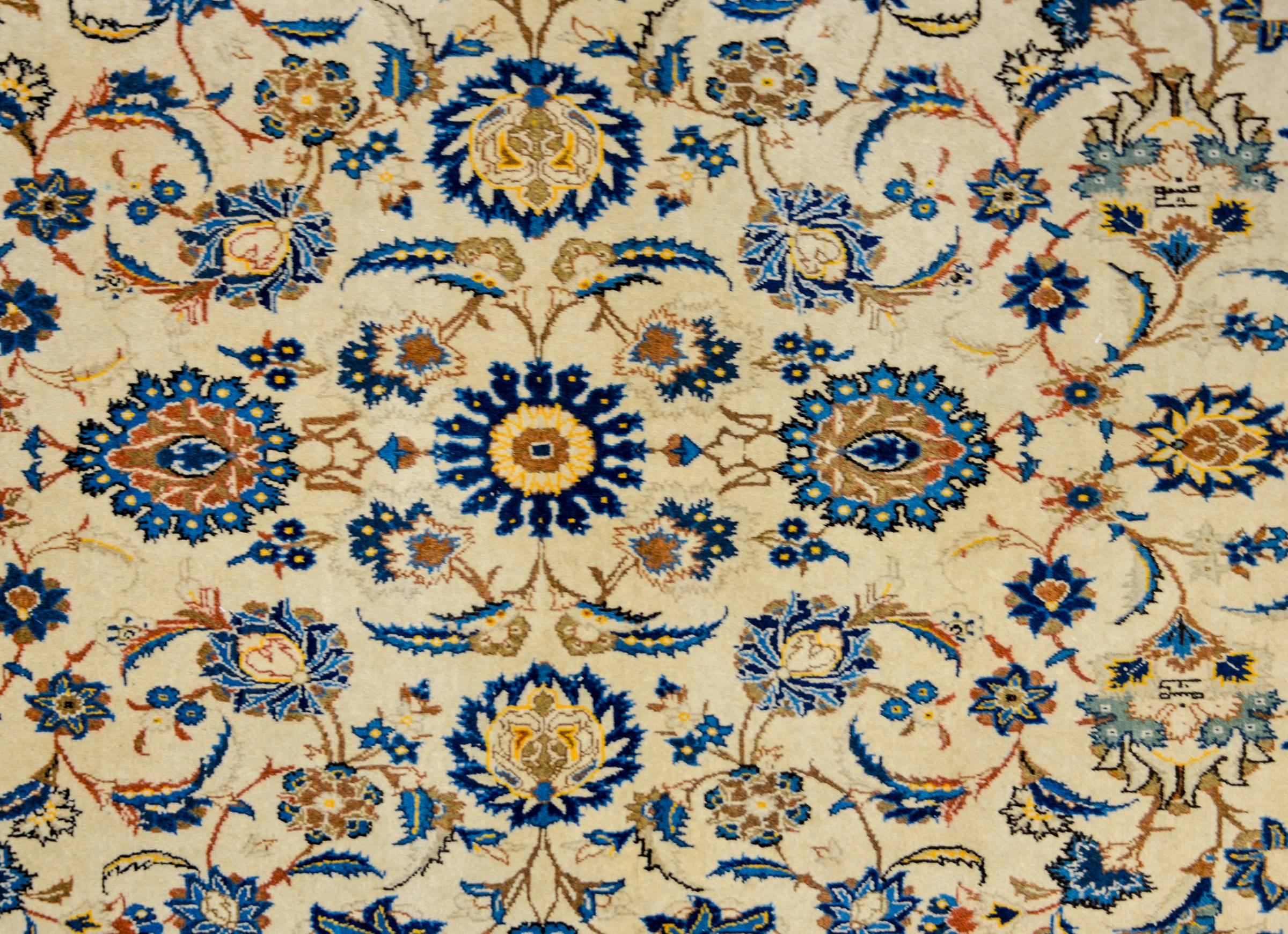 A fantastic early 20th century Persian Kashan rug with a wonderful all-over mirrored floral and vine pattern woven in light and dark indigo, gold, and brown vegetable dyed wool, on a cream colored wool background. The border is complimentary, woven