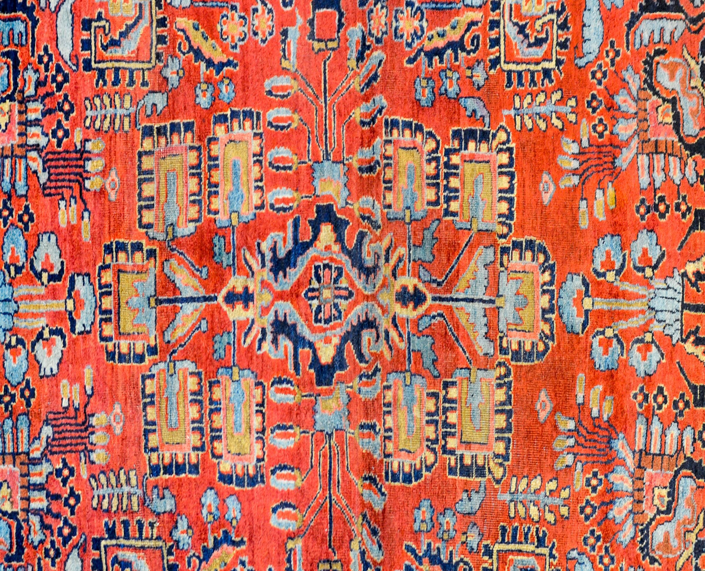 An amazing early 20th century Persian Sarouk rug with a brilliant crimson background, covered by a lacy, multicolored mirrored scrolling vine and floral pattern, surrounded by a wide indigo border with a large-scale floral pattern.