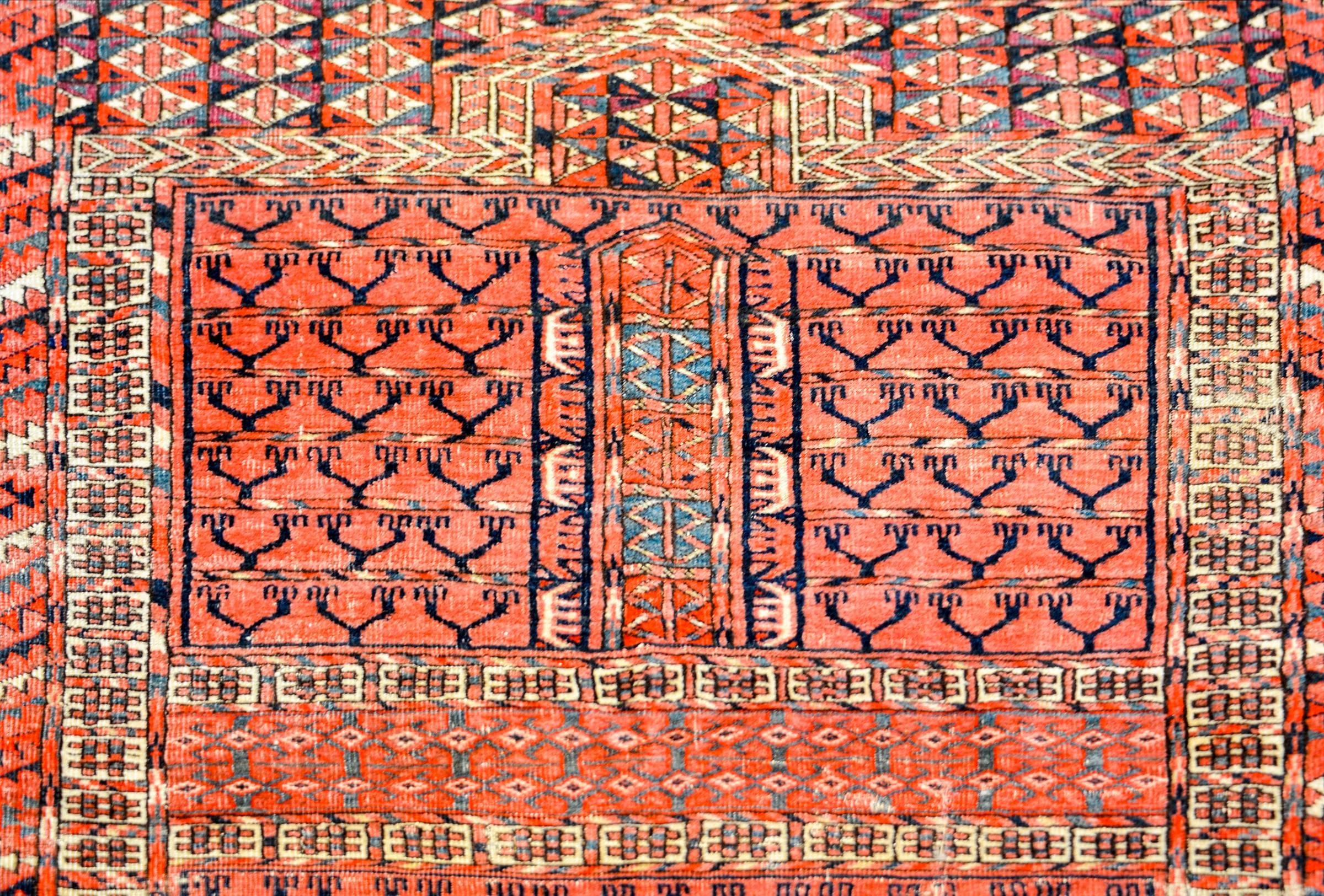 A 19th century Persian Turkmen prayer rug with a beautiful elaborate geometric pattern in alternating colors of crimson, indigo, coral, and cream, surrounded by a multiple elaborate complementary borders.